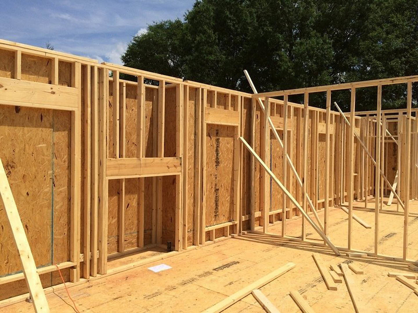 Exposed wooden framing and beams of a house under construction against a blue sky with scattered clouds