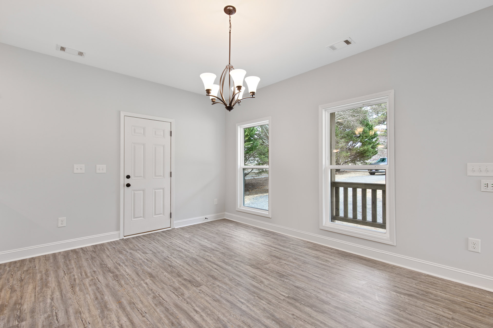 Wood floor room with white walls, black-knobbed white door, modern chandelier, window showing tree and parked car outside