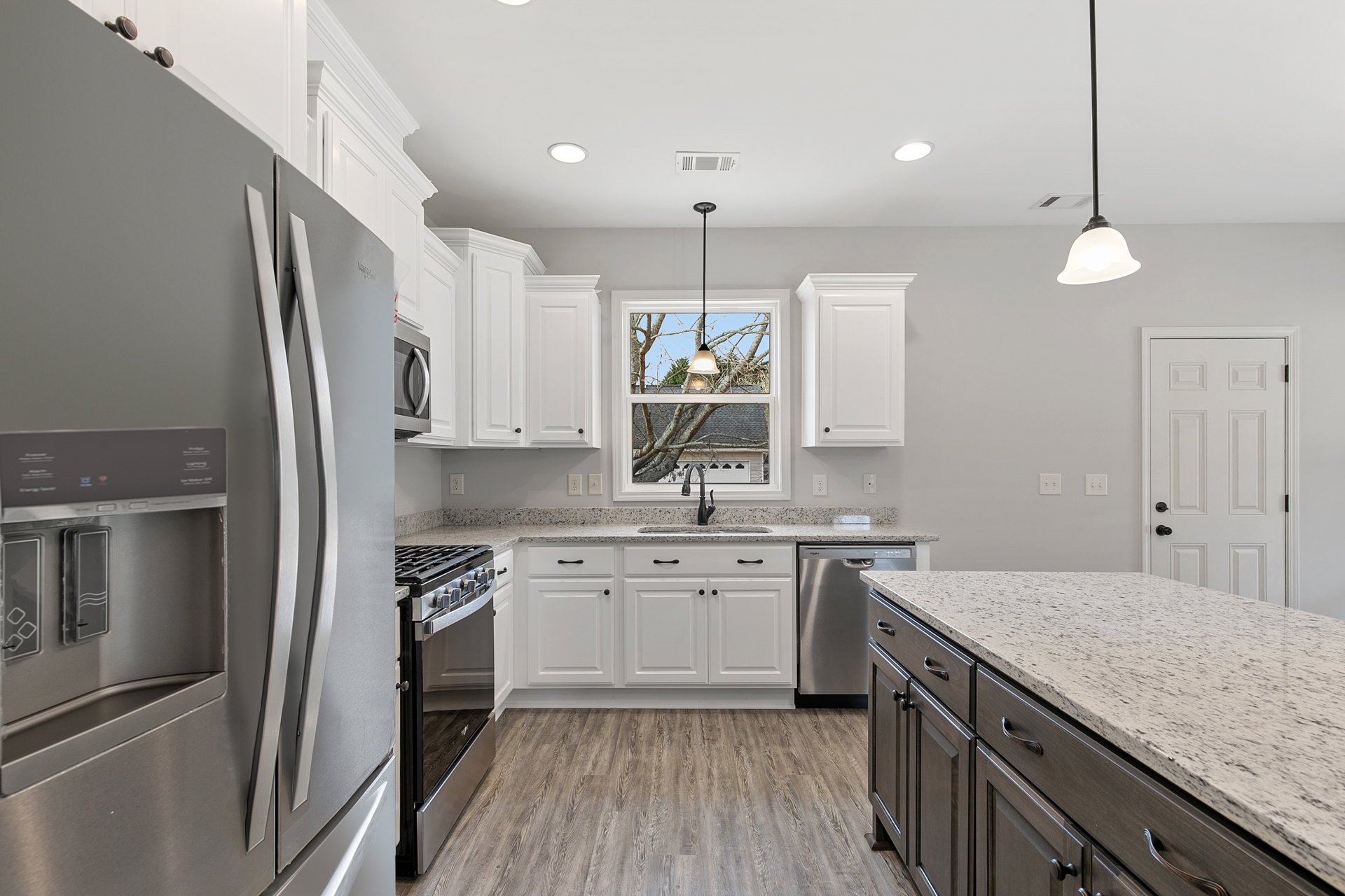 Kitchen with white shaker cabinets, speckled granite countertops, stainless steel sink, and black hardware; window provides natural light, white door with black handles visible in