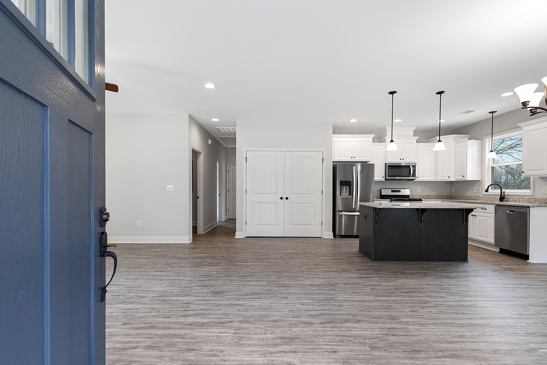 Open kitchen and living room featuring wide plank wood flooring, white cabinetry, black kitchen island with marble countertops, stainless steel refrigerator with ice and water