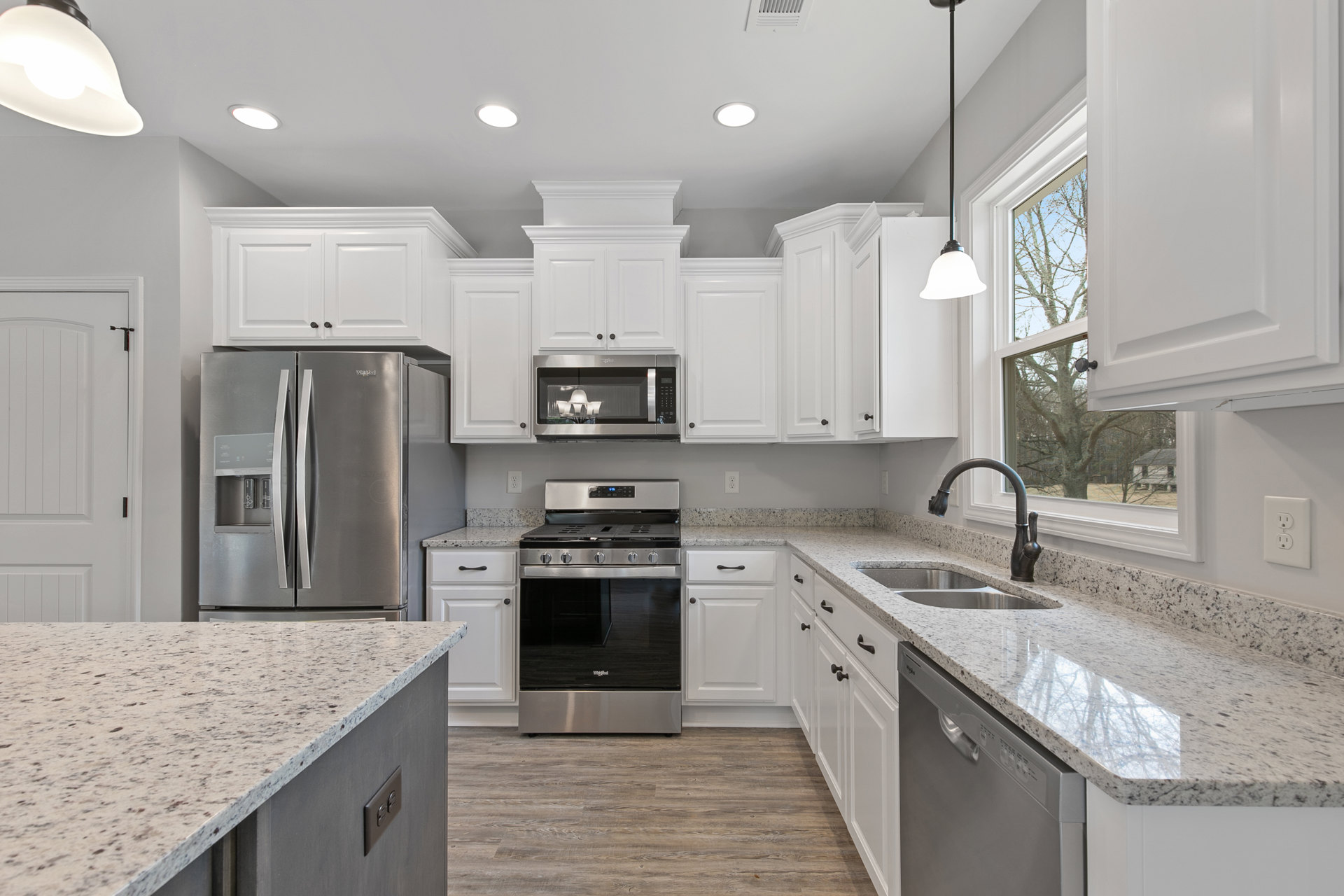 White cabinetry and speckled granite countertops in a kitchen with stainless steel double-door refrigerator, black stove, built-in microwave, and modern light fixture