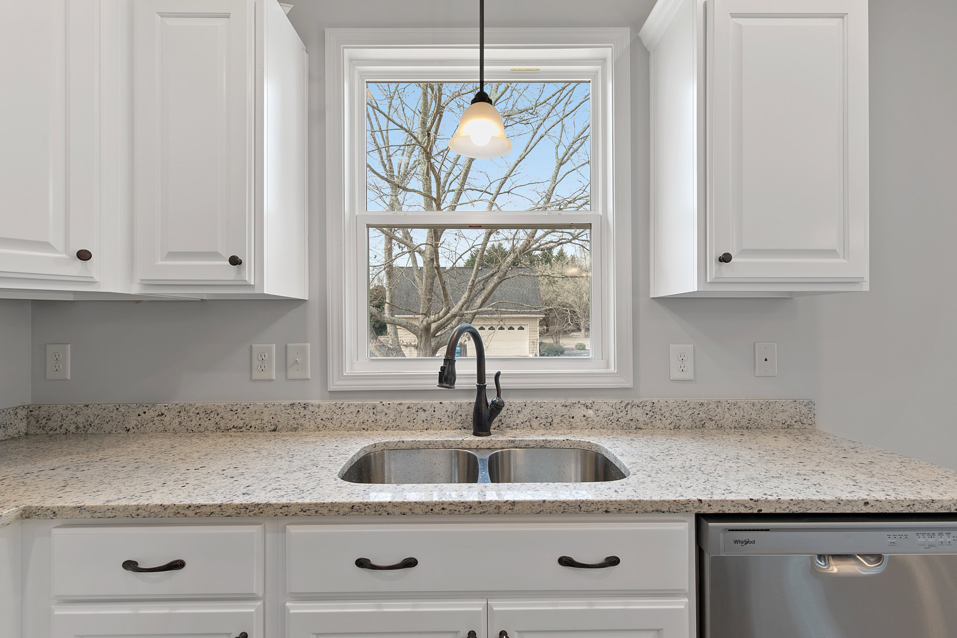 White kitchen with stainless steel sink under a large window, quartz countertop, shaker cabinetry, chrome faucet, and pendant light fixture
