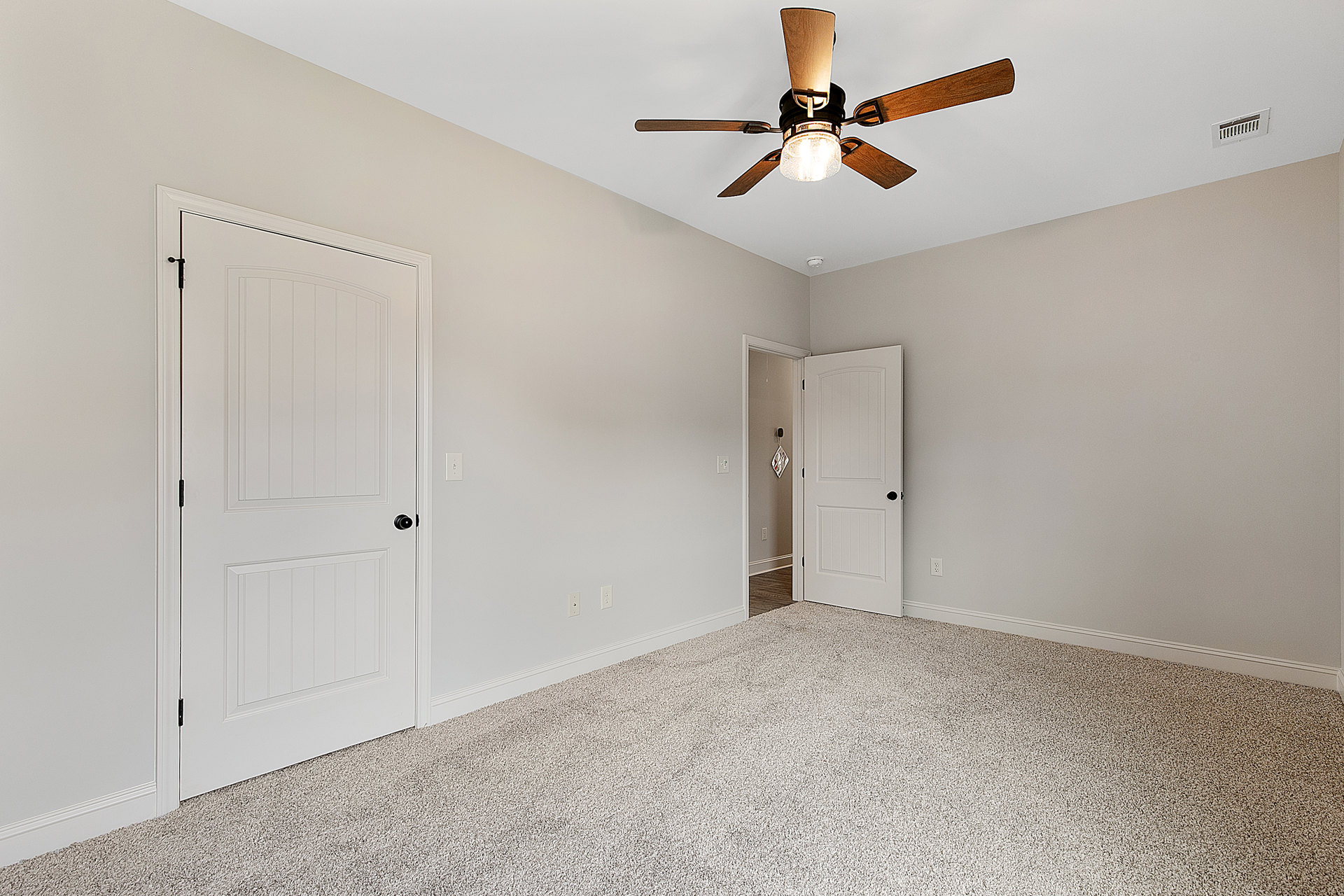 Carpeted room with a ceiling fan and light, two white doors with black hardware, white walls, and plaster ceiling