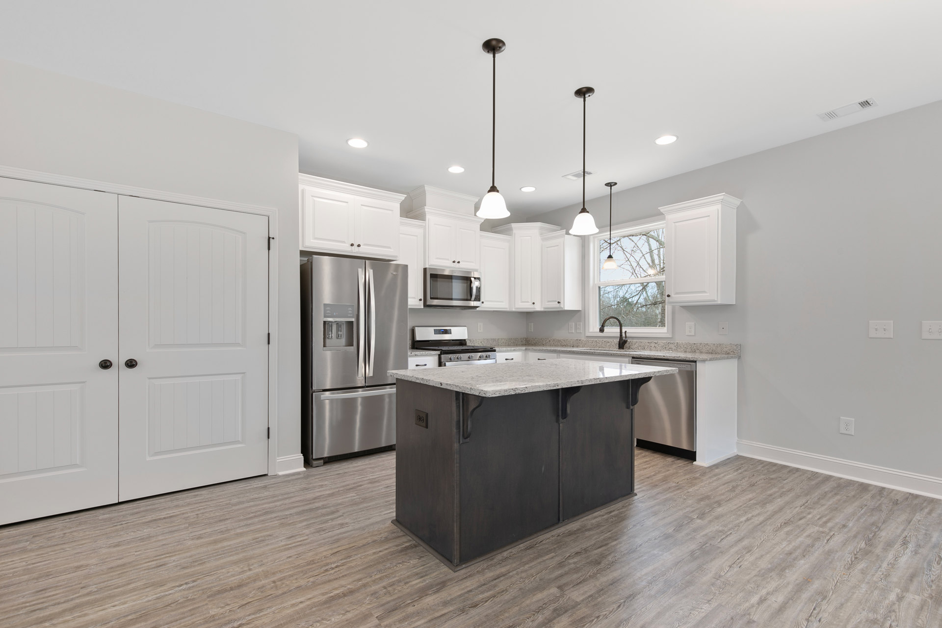Spacious kitchen featuring a large central island with built-in stove and oven, stainless steel double-door refrigerator, white cabinetry, tile backsplash, undermount sink, pendant