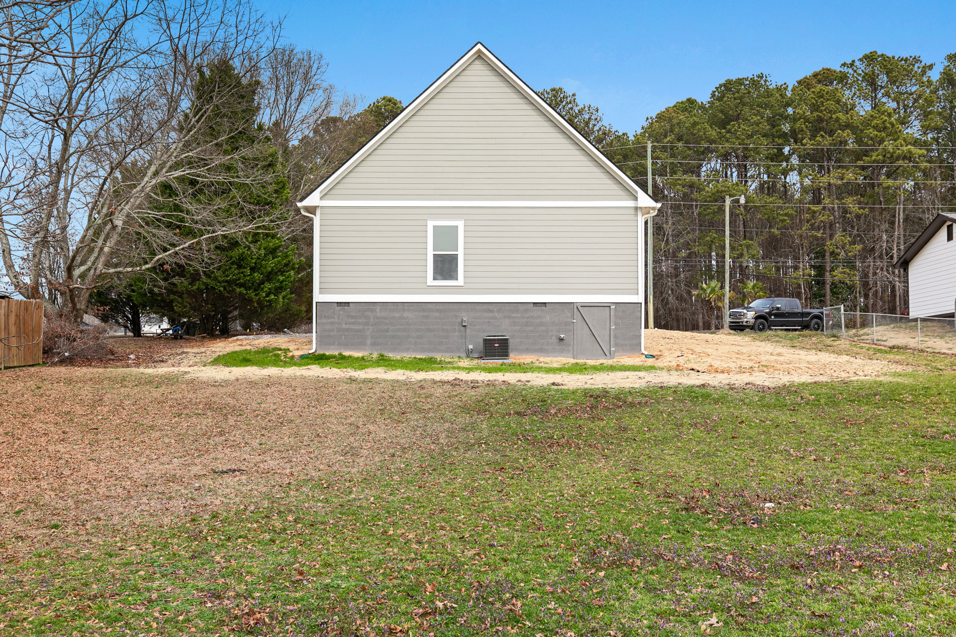 Two-story house with white-framed windows, attached garage, black truck parked on driveway, large air conditioner unit, surrounded by grass lawn and mature trees