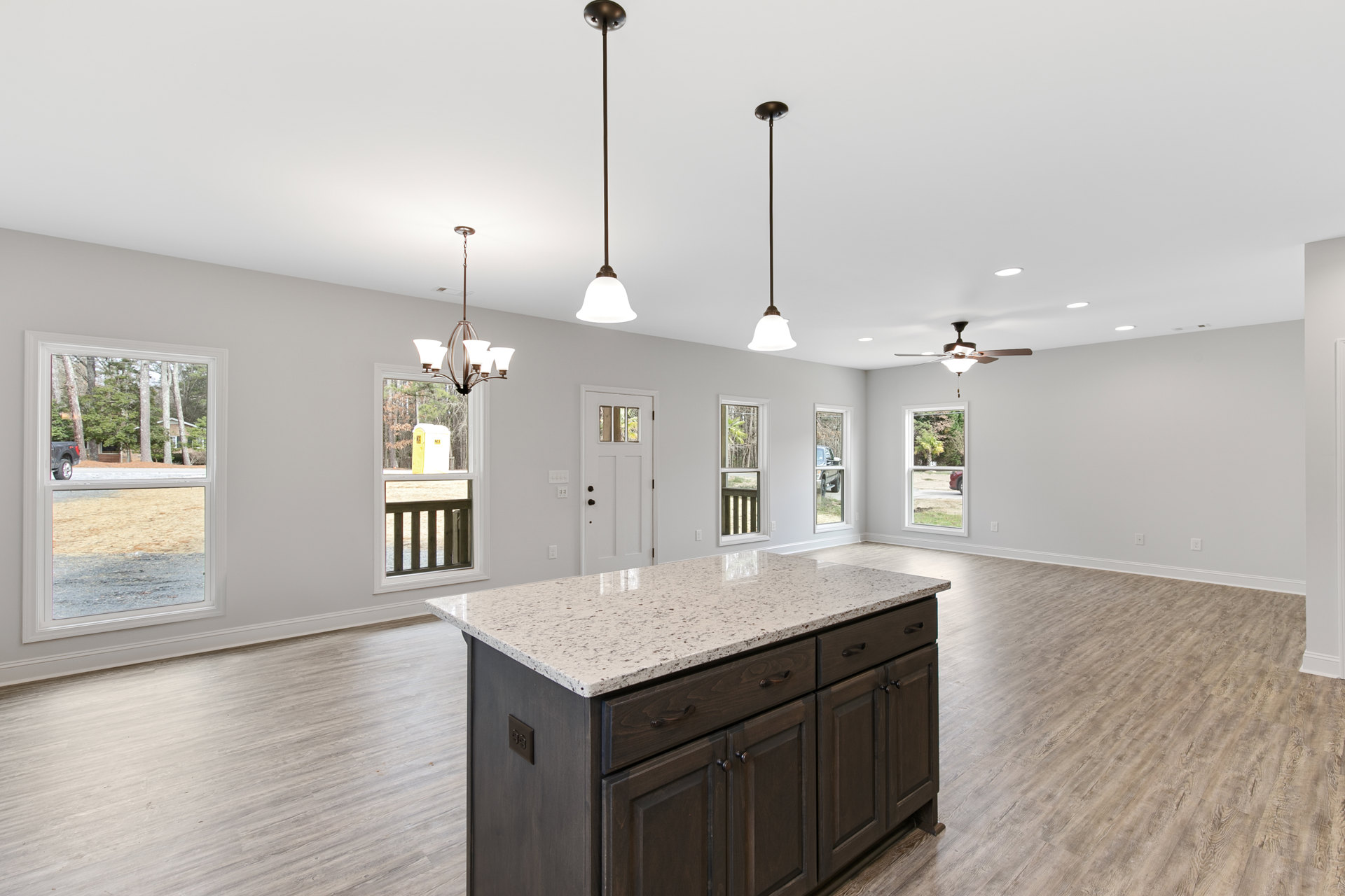 Marble-topped kitchen island with built-in sink and faucet, surrounded by tile flooring, cabinetry, and a window with wooden railing overlooking trees; pendant light fixture