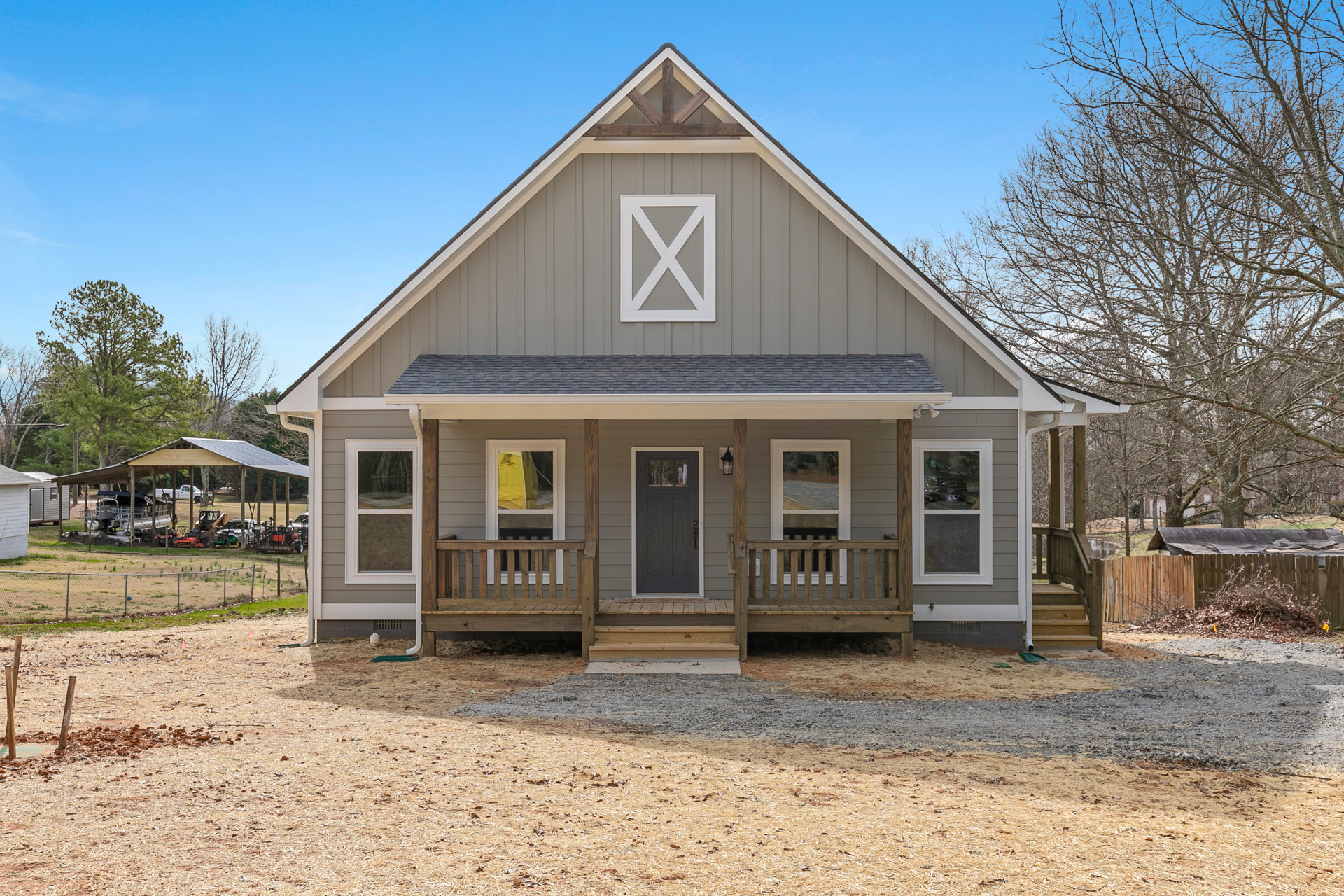 Modern home with gray siding, black front door with window, covered porch, concrete driveway, yellow portable toilet visible through window, white X marking on wall, landscaped