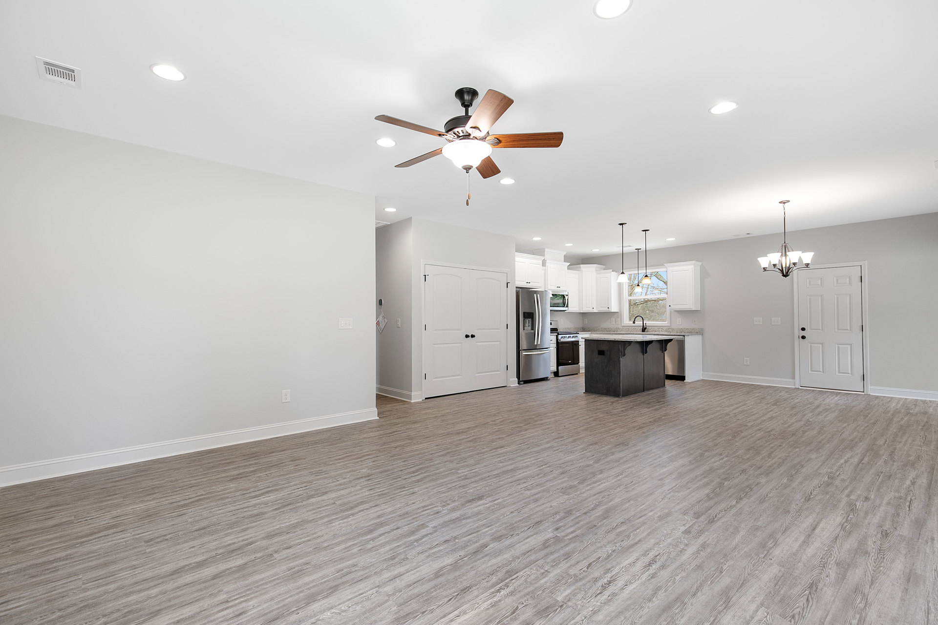 Open-concept kitchen with wood flooring, white cabinetry, stainless steel refrigerator, ceiling fan with light fixture, and white doors featuring black handles and knobs