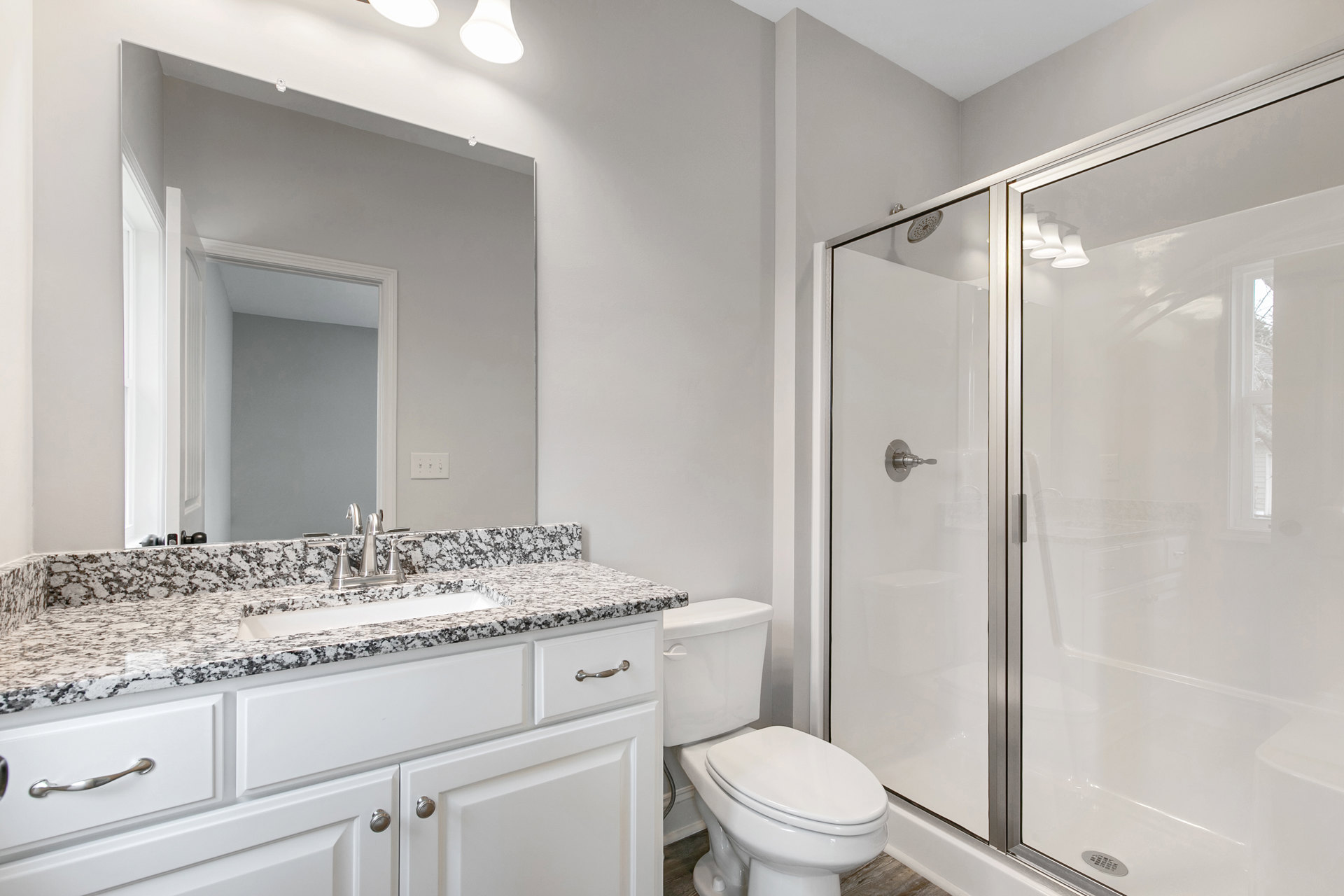 Bathroom with marble countertop, undermount sink and chrome faucet, glass-enclosed shower with tile walls, white toilet, and modern hardware