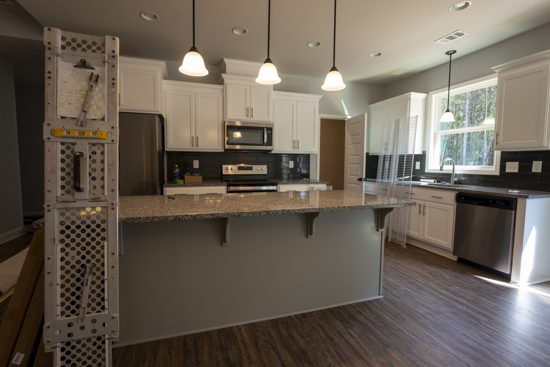 Granite countertop kitchen with stainless steel refrigerator, wood flooring, white cabinetry, built-in microwave, and modern stove.
