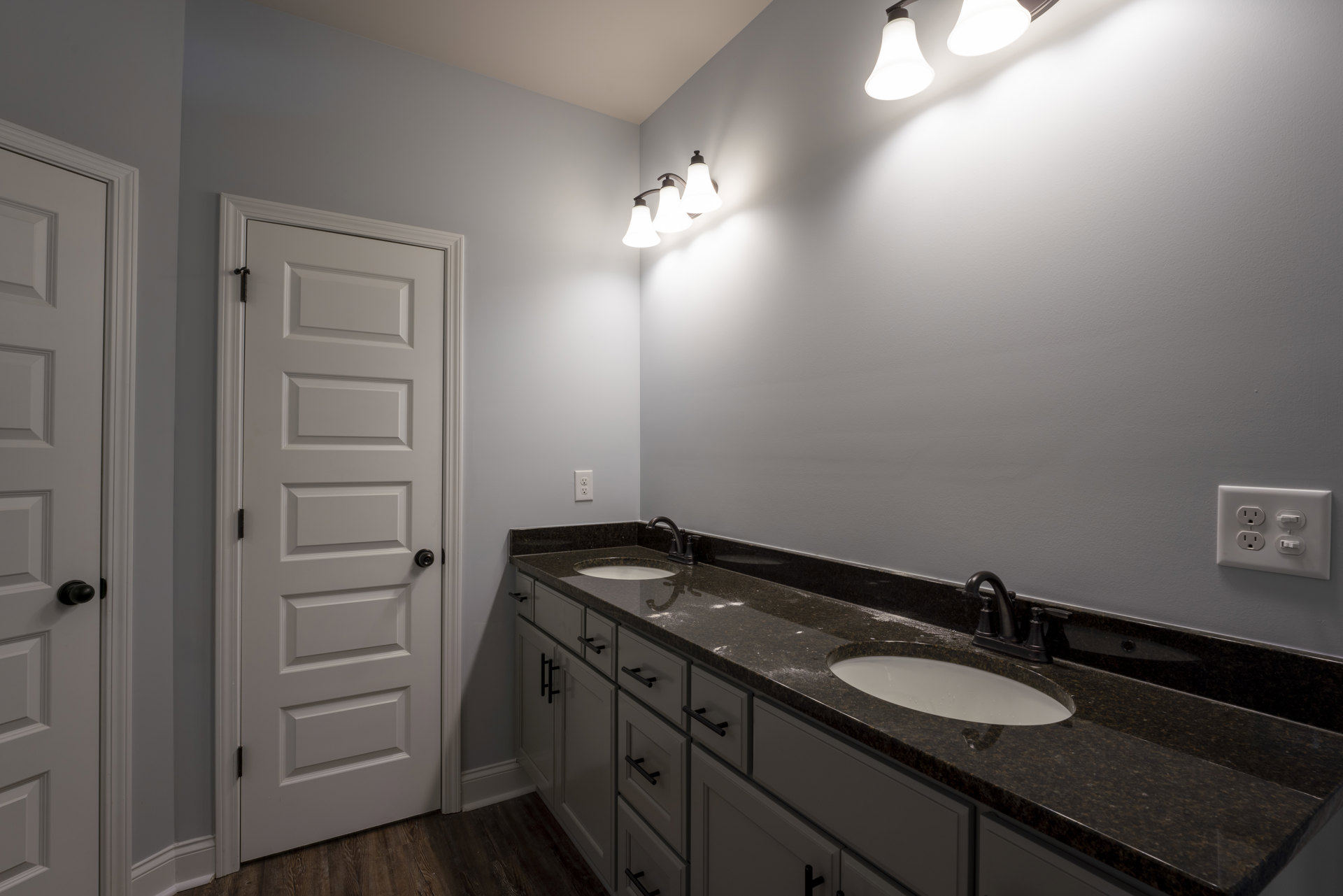 Double vanity bathroom with white sinks, black faucets, light gray tile backsplash, white cabinetry, quartz countertop, and a white door with black hardware