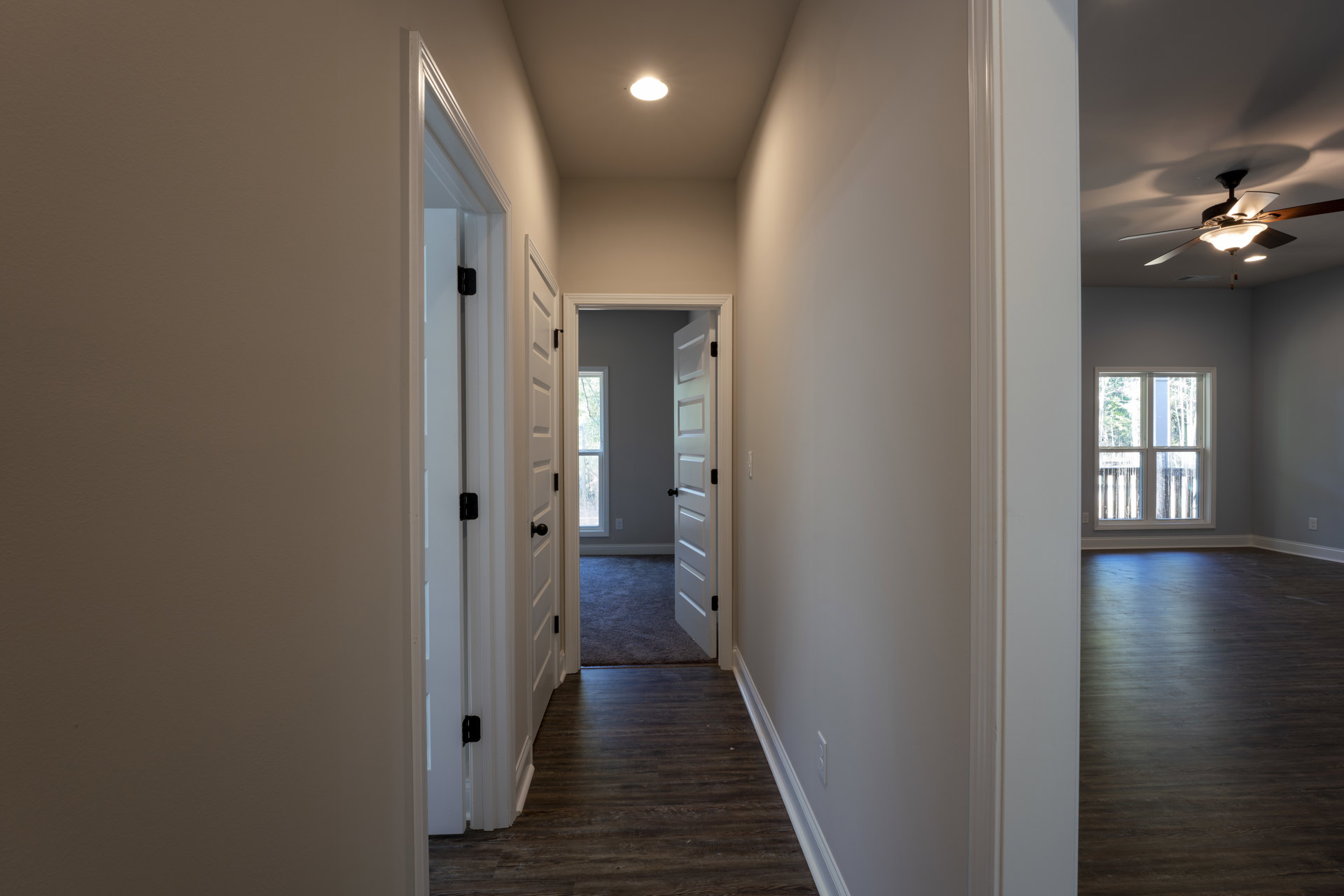 Hallway with white plaster walls, dark wood flooring, ceiling fan with light fixture, recessed ceiling light, window with glass panel overlooking trees