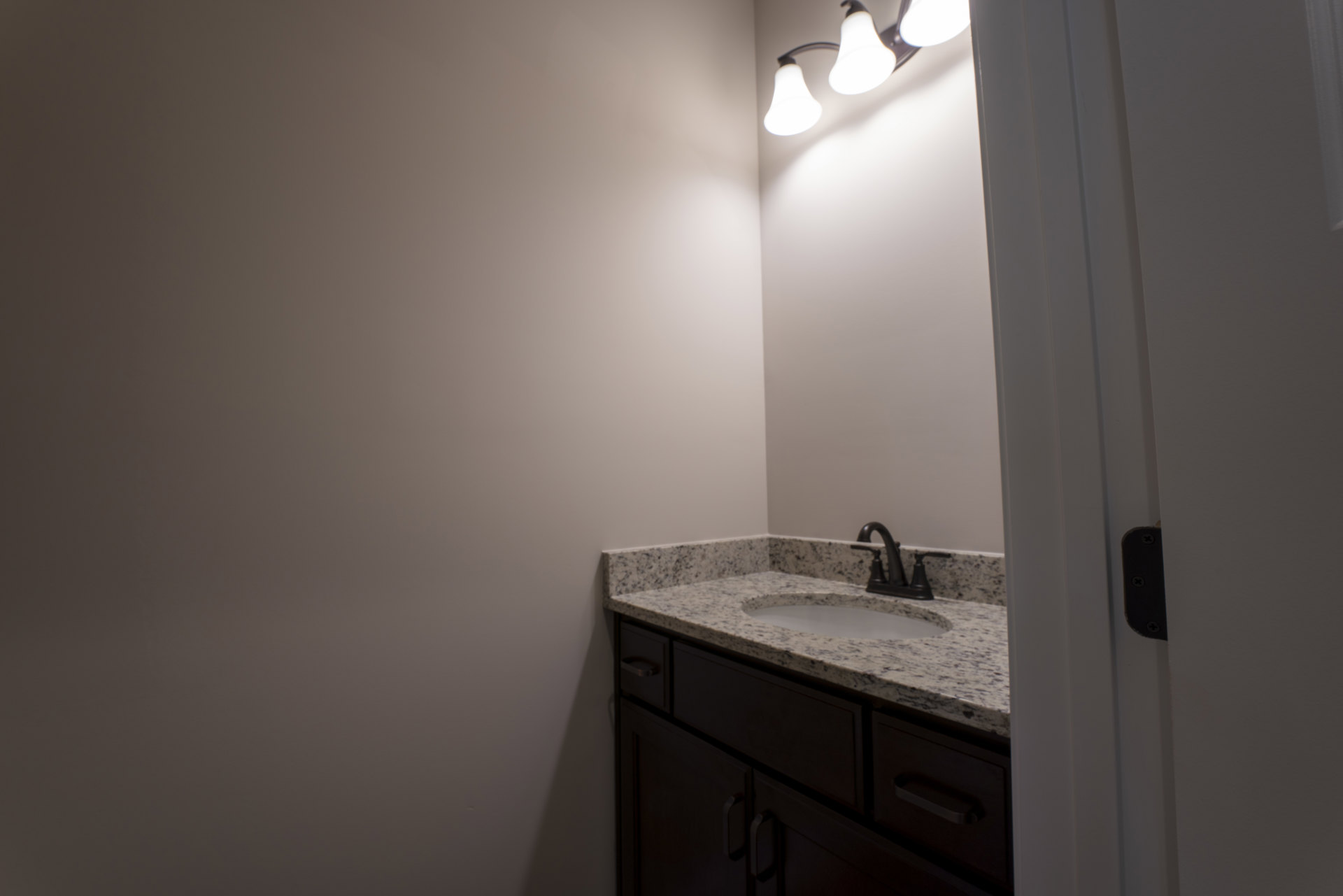 Marble countertop with undermount sink and matte black faucet, white tile backsplash, light fixture reflected in mirror, cabinetry with brushed metal hardware