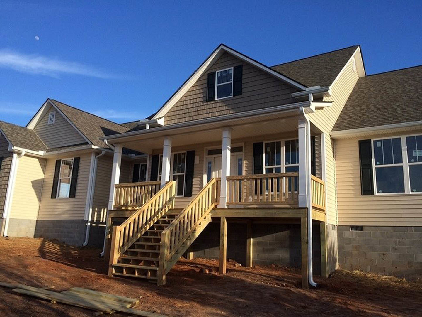 White-framed window above wooden porch with exterior stairs, horizontal siding, and shingled roof under blue sky