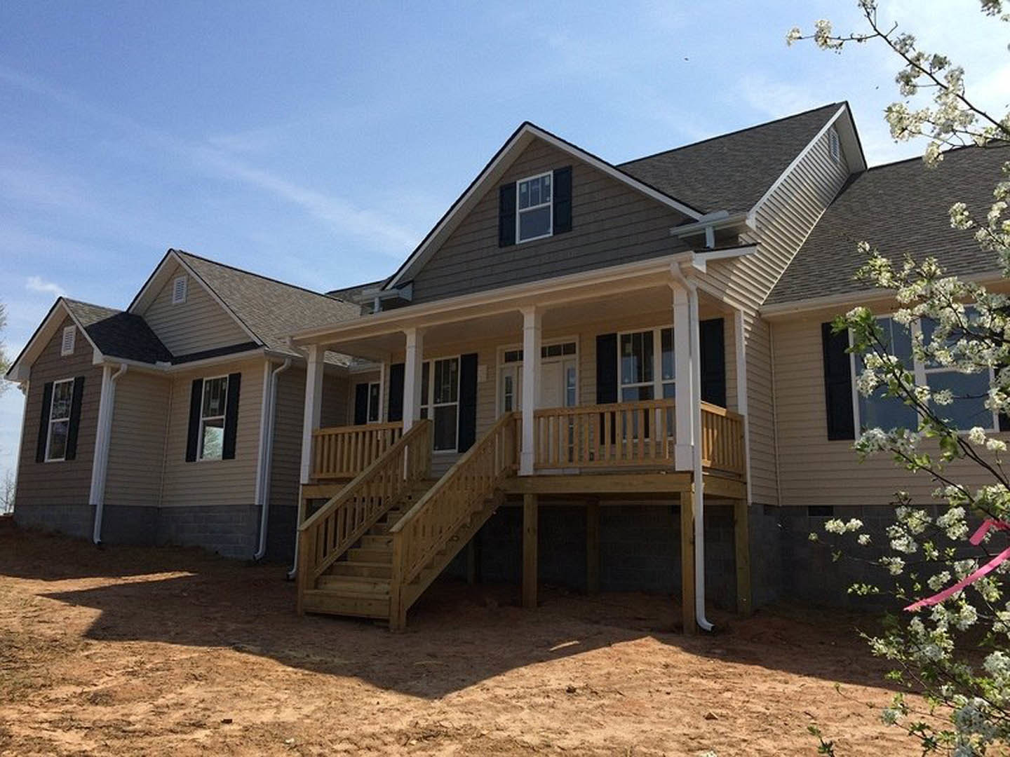 White house with wooden porch and stairs, large window, blooming tree with white flowers, blue sky in background