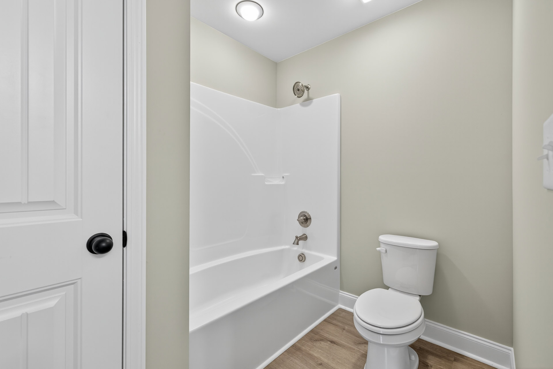 White tile bathroom with built-in bathtub, chrome faucet and knobs, white toilet, plaster walls, and black door knob