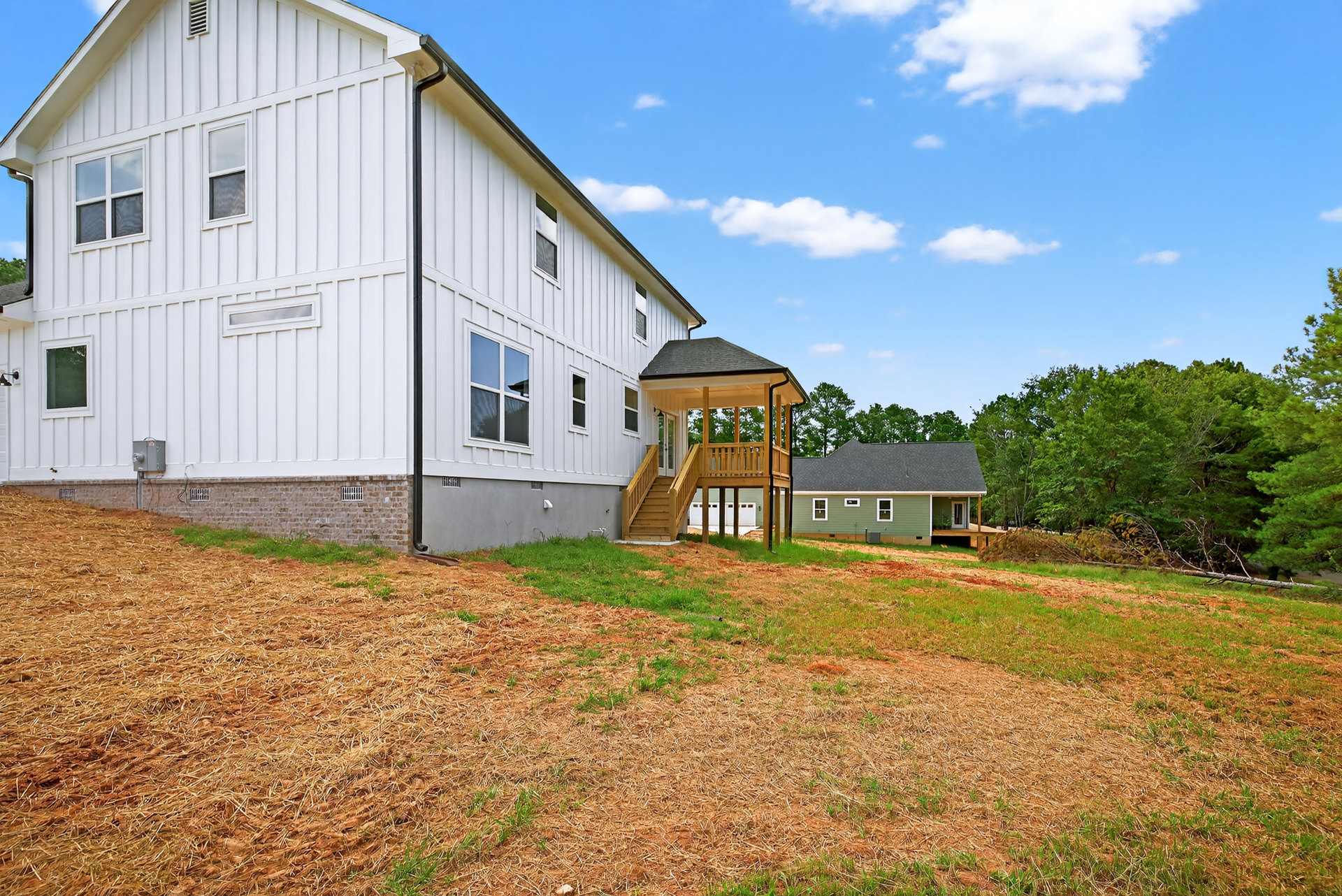 White farmhouse with covered wooden porch, manicured lawn, attached garage, large windows, and blue sky overhead