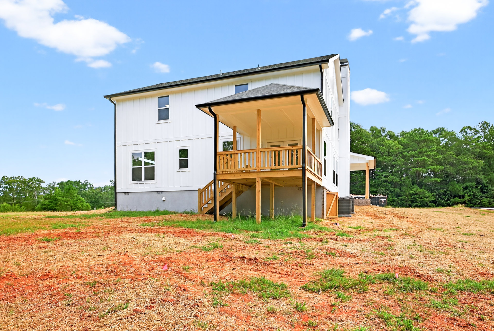 White house with two porches, wooden deck, large grey planter, grassy yard, trees, and cloudy sky