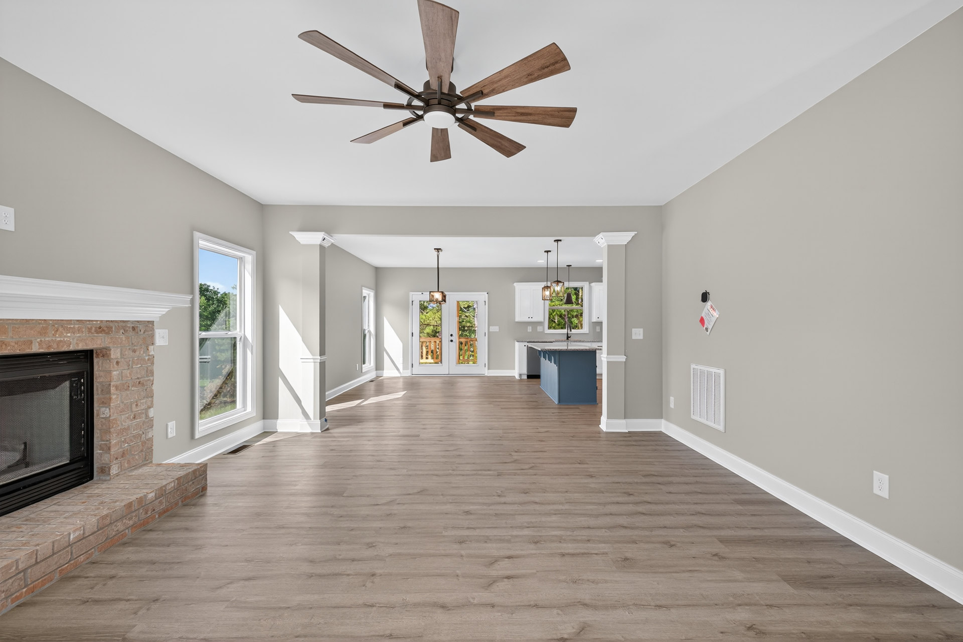 Spacious living area with wood flooring, ceiling fan with wood blades, double doors, fireplace, and large window overlooking trees
