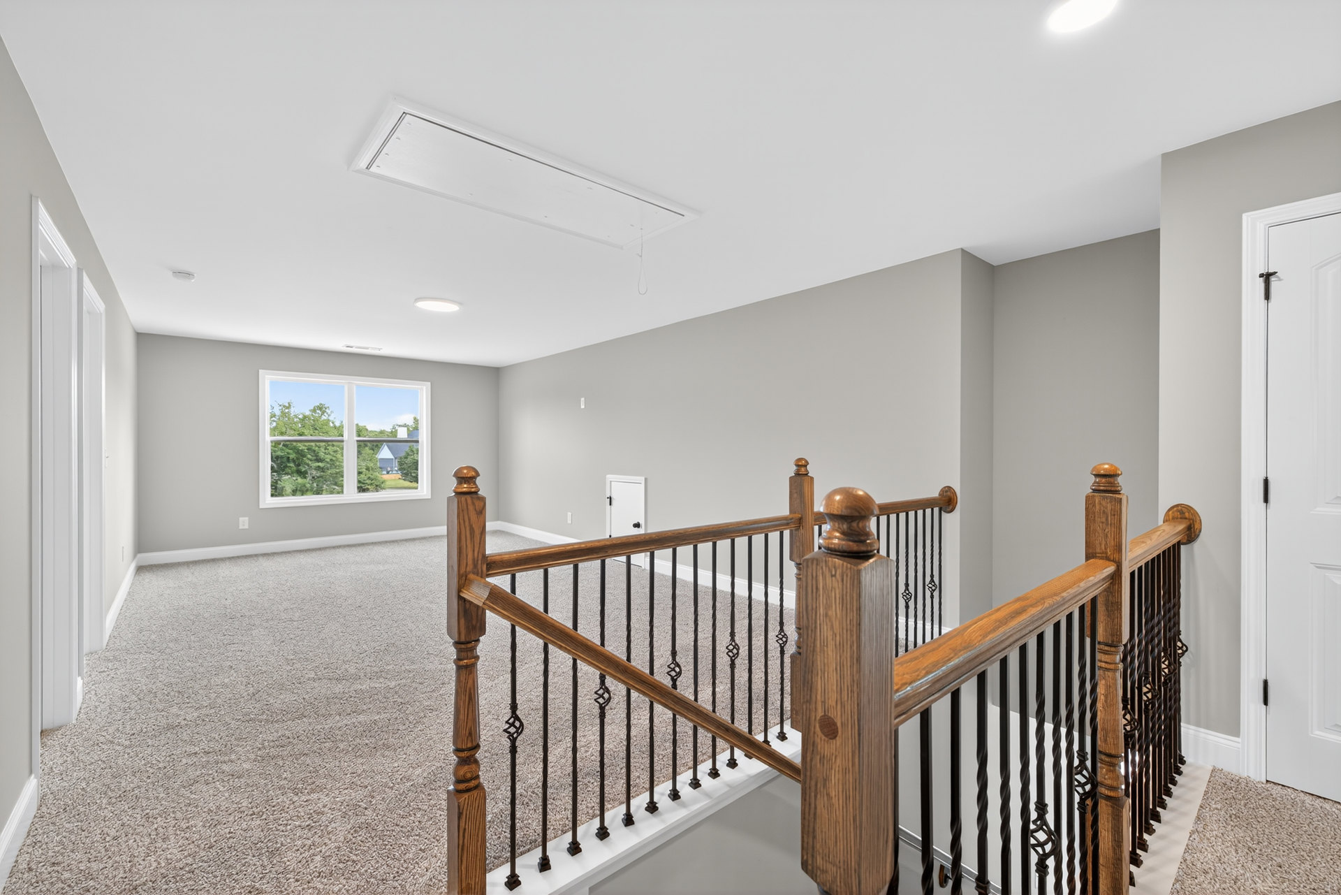 Wooden staircase with matching handrail and balusters, large window overlooking trees, plaster walls, hardwood flooring, and visible door hinge.