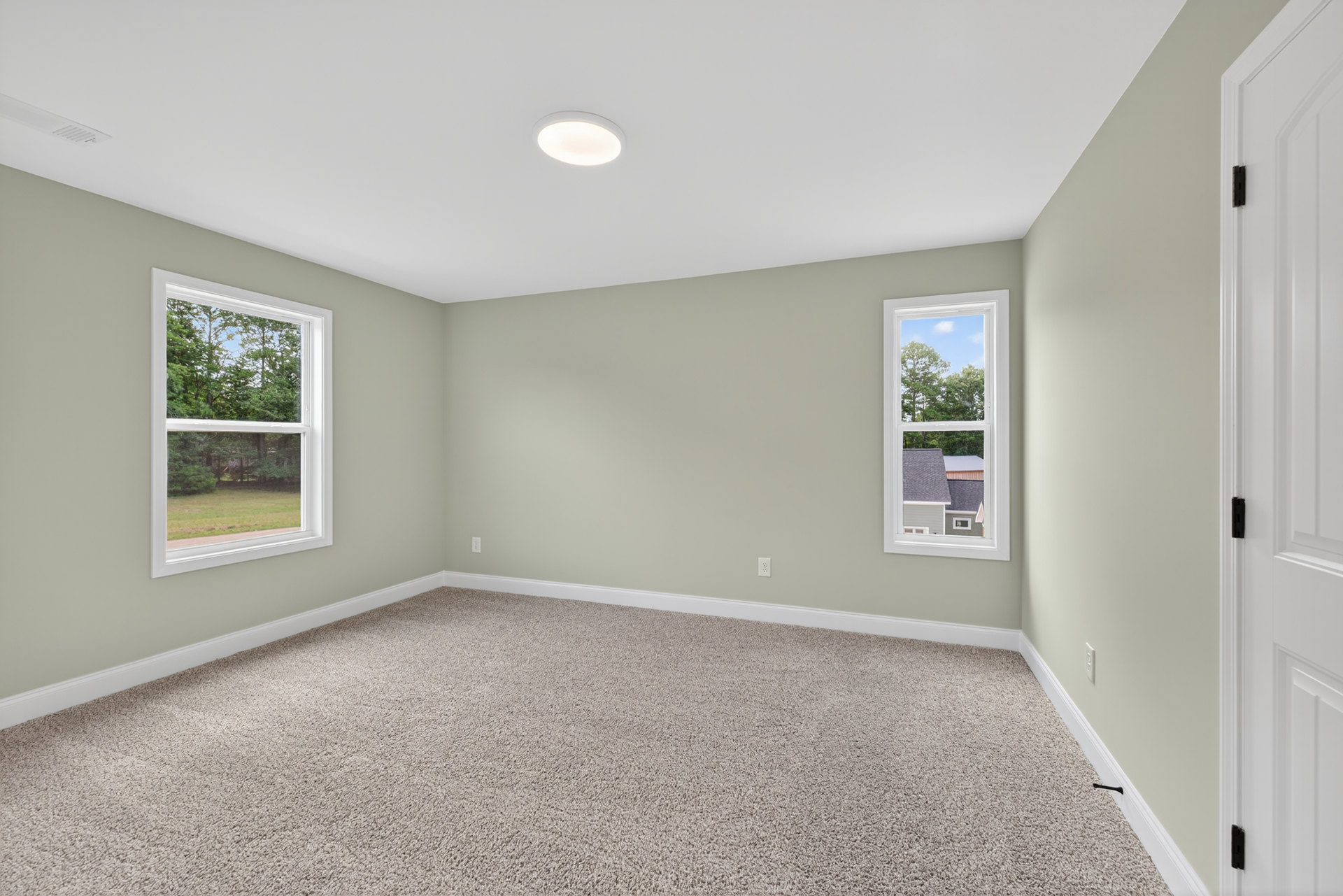 Carpeted room with large windows, white walls, and ceiling light fixture; view of trees visible through windows