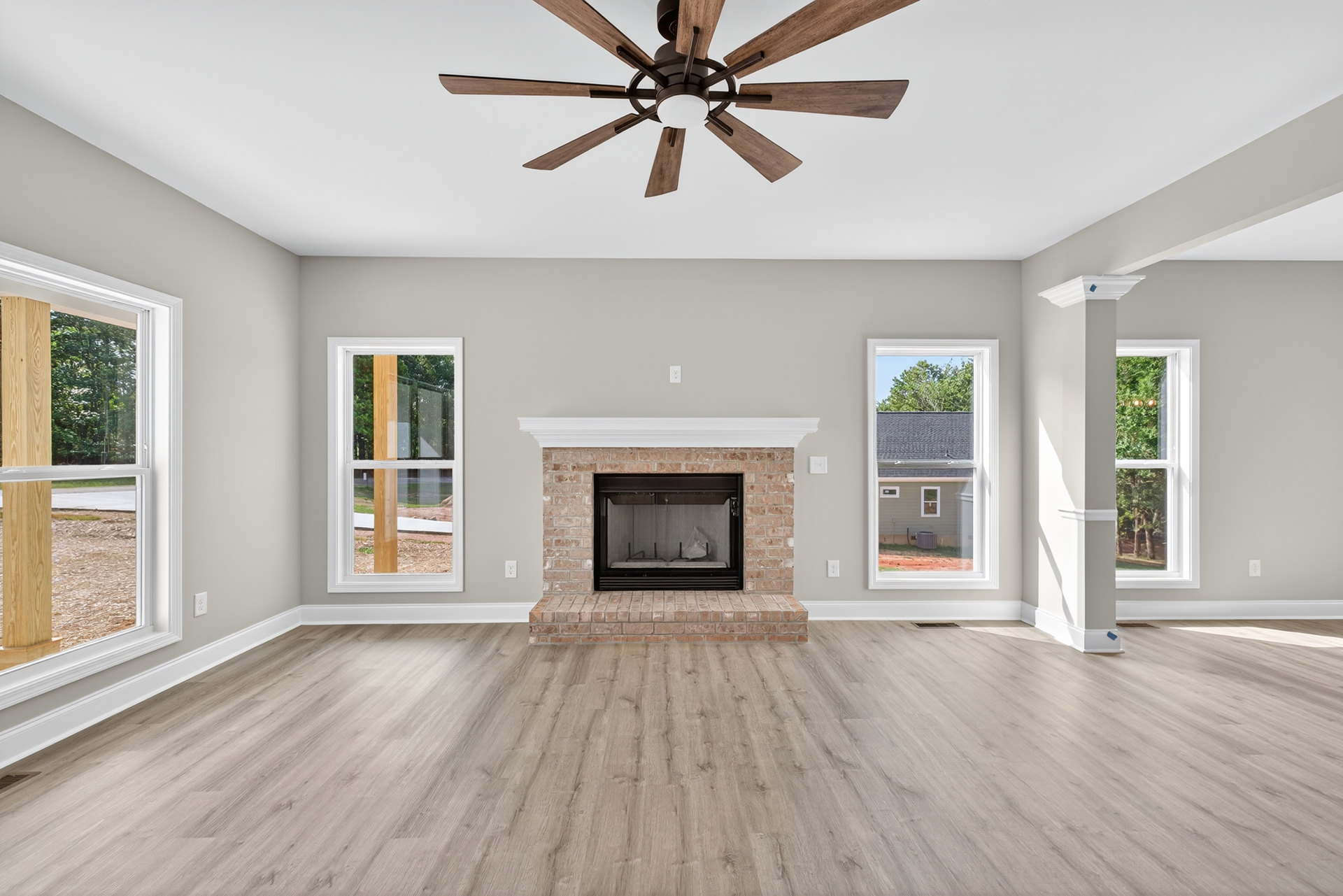 Living room with wood flooring, brick fireplace with glass door, ceiling fan with light, white walls, and crown molding