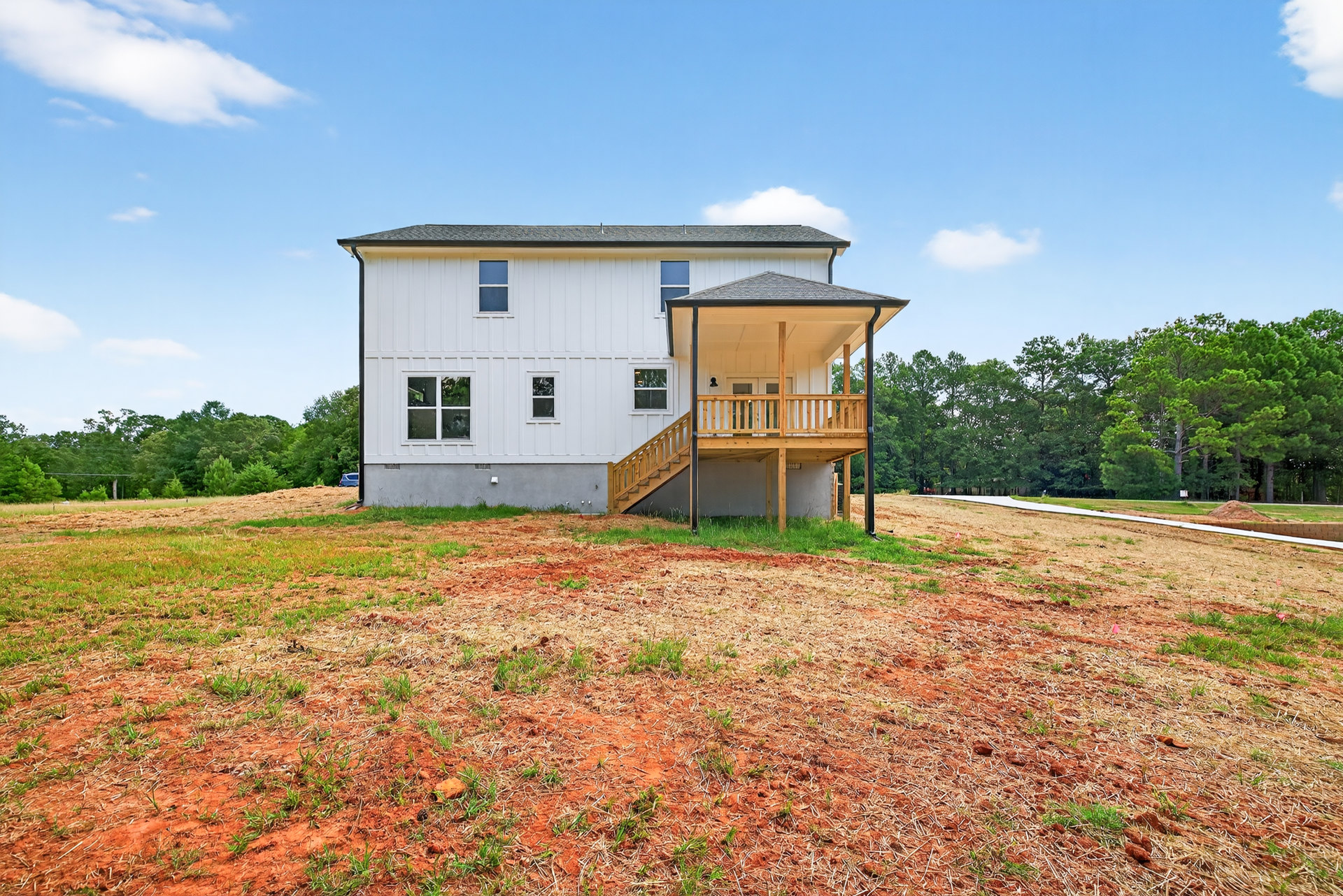 White siding house with covered front porch, wooden deck, stairs leading to grassy yard, light post, blue sky with scattered clouds
