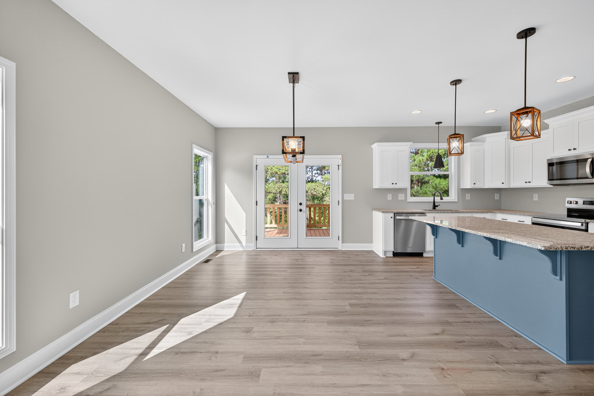 Kitchen with wood flooring, granite-topped island, white cabinetry, double glass-paneled doors, stainless steel microwave, pendant light fixture, and white door.