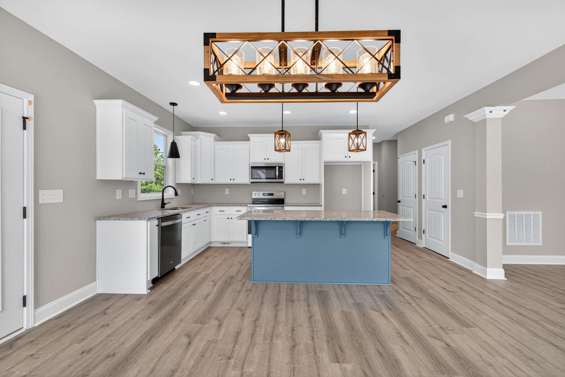 Open kitchen with wood flooring, central island featuring stone countertop, blue accent wall, glass and metal pendant lights, white cabinetry, stainless steel microwave, and