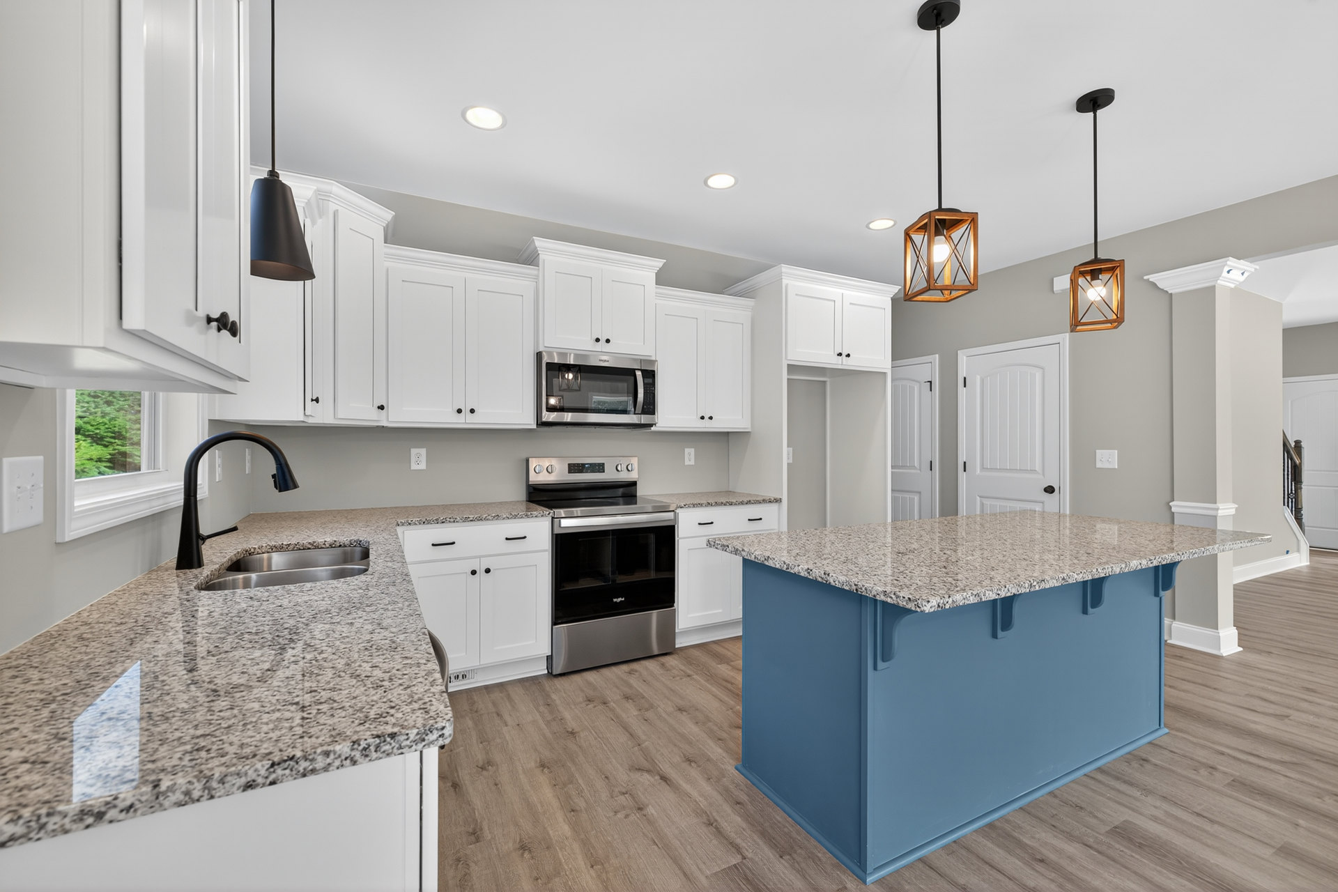 Granite countertops, blue kitchen island with marble top, stainless steel oven and stove, built-in microwave, wood-framed light fixture, white cabinetry, tile flooring