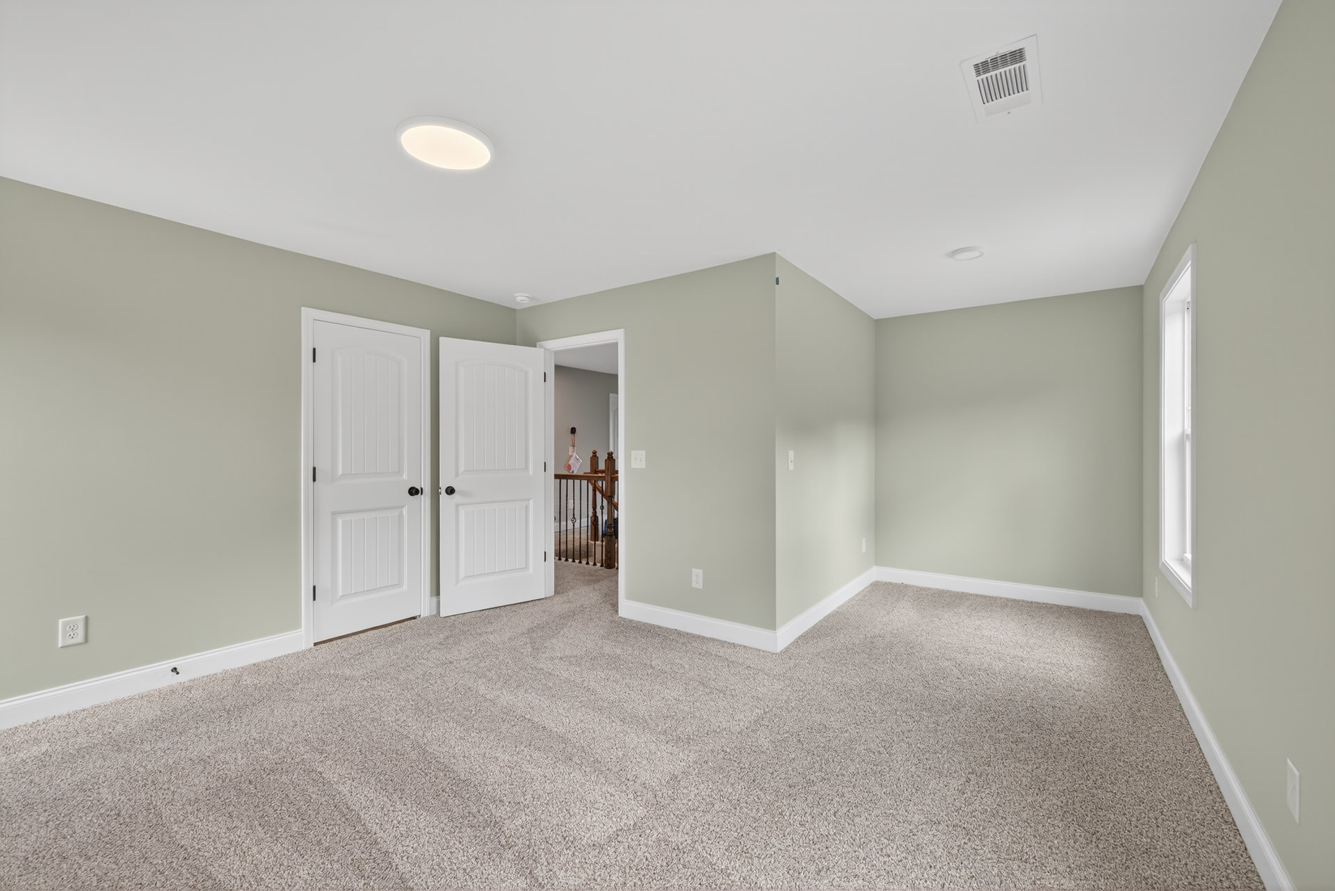 Carpeted room with white paneled doors featuring black knobs, white walls, ceiling vent, and recessed light fixture