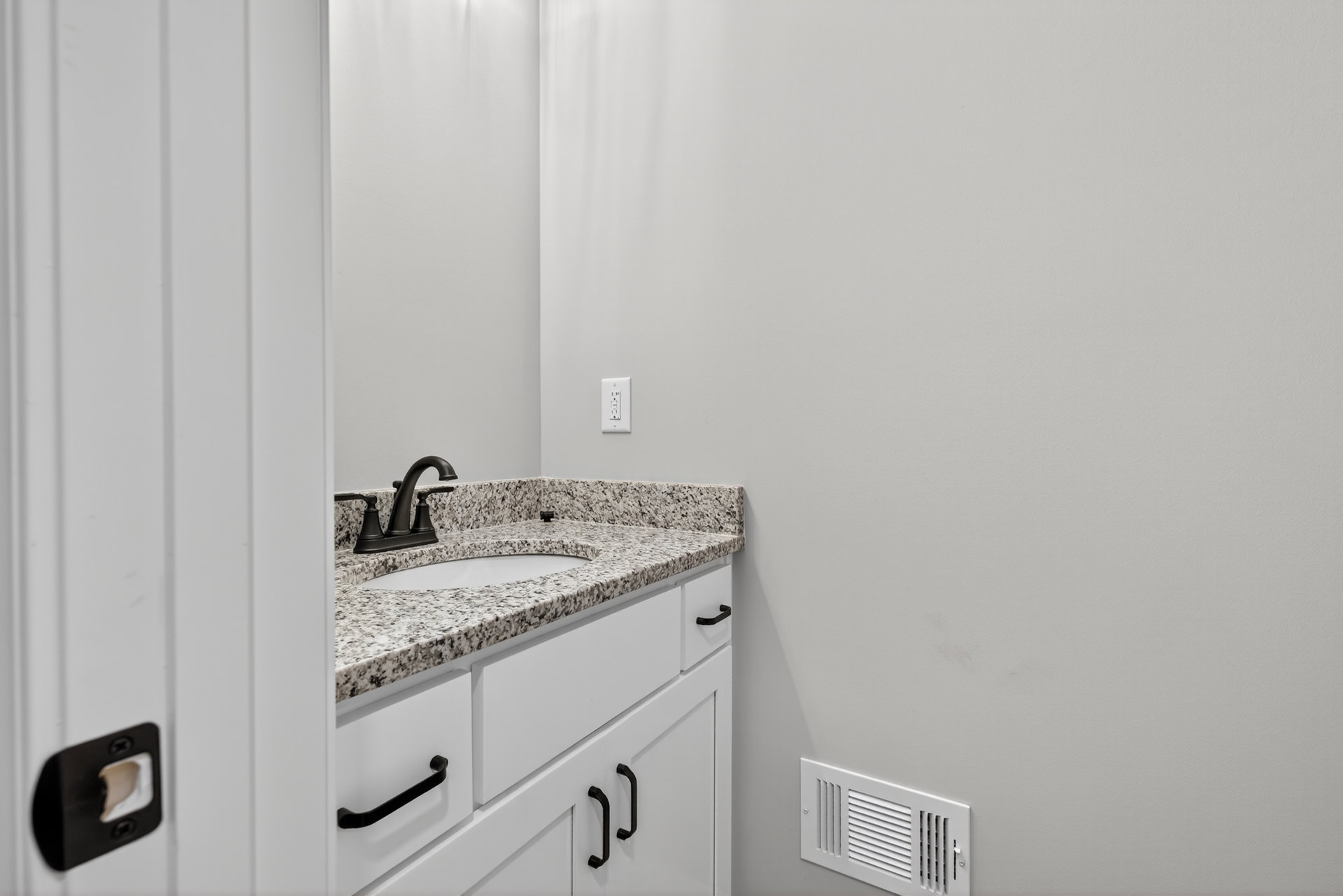 Marble countertop with black faucet and undermount sink, white cabinetry below, large mirror above, white tile walls, visible wall vent and small hole in wall