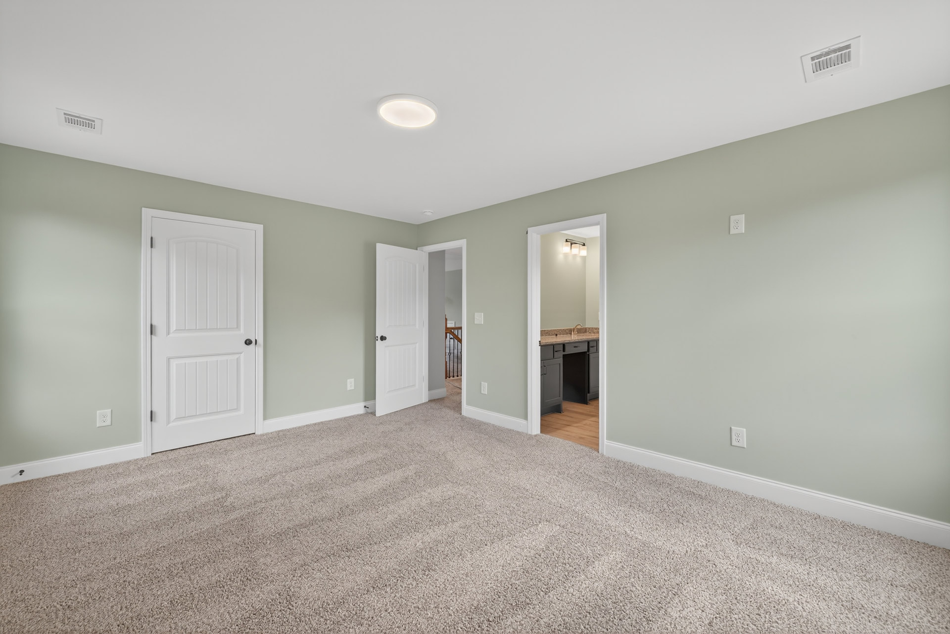 Carpeted room with multiple white paneled doors featuring black hardware, white walls, ceiling vent, and recessed light fixture