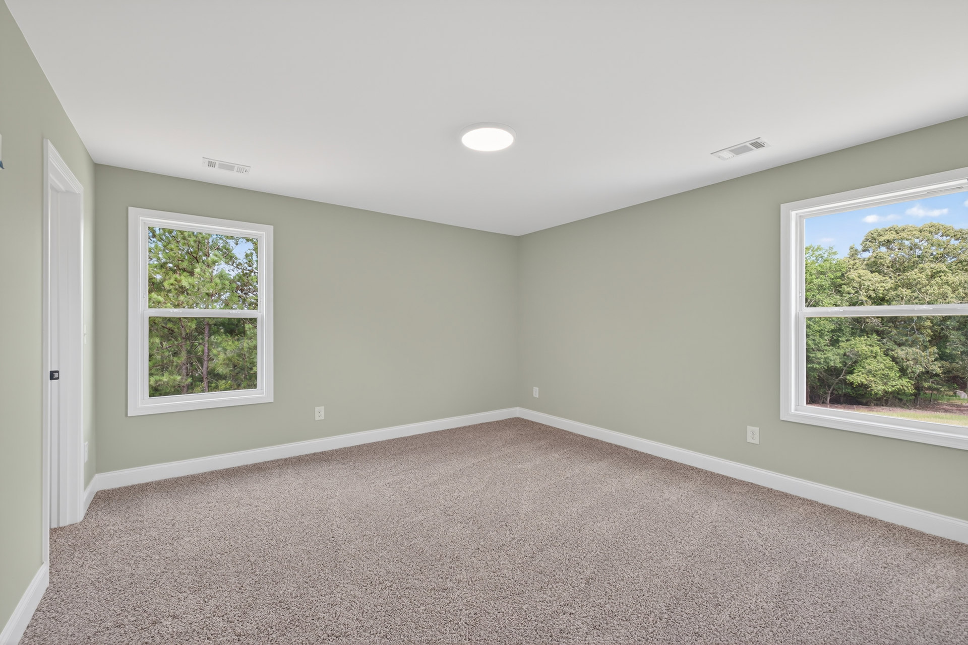 Carpeted room with large windows, white walls, and ceiling light fixture; trees visible through window.