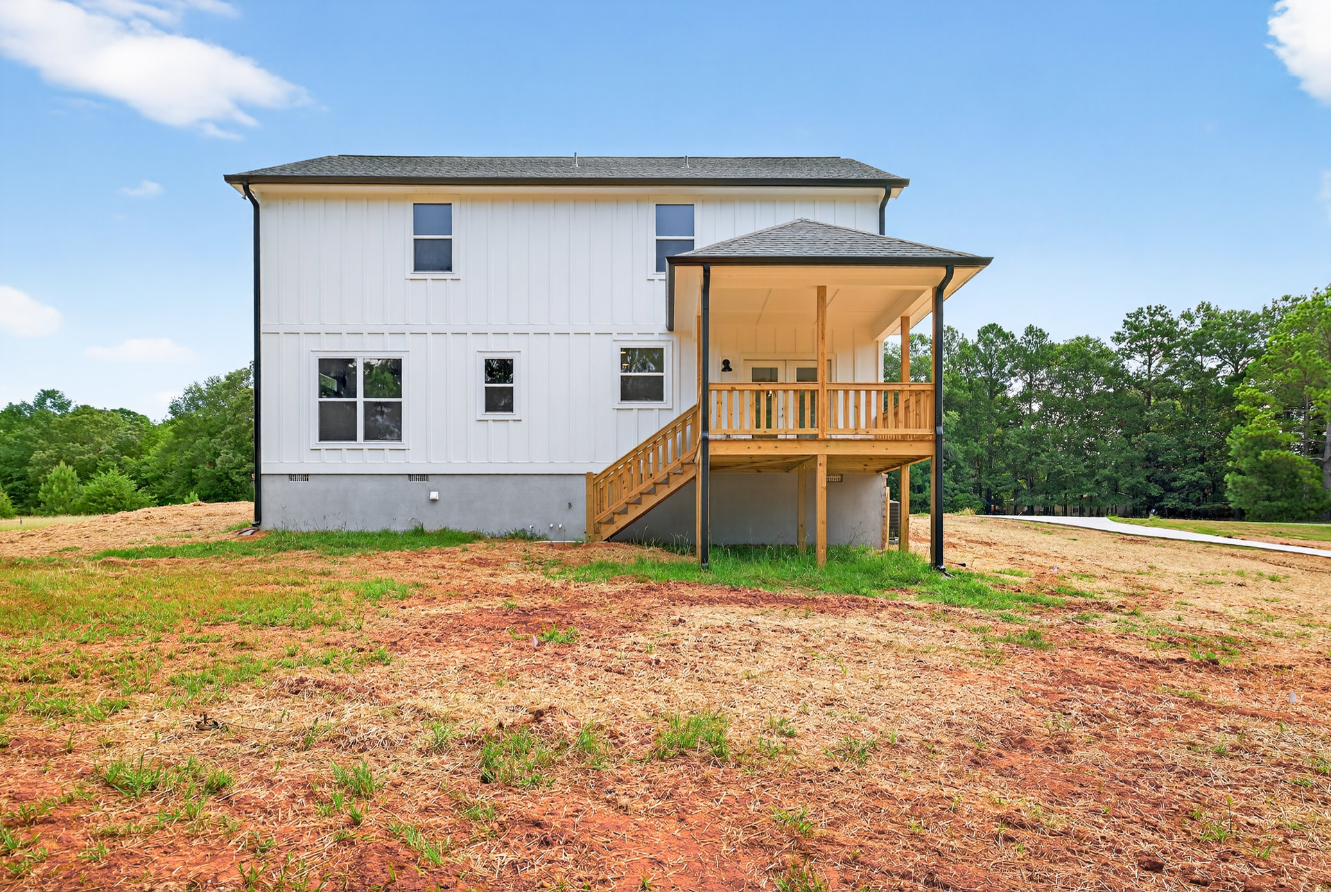 White house with two covered porches, wooden deck flooring, large windows, surrounded by grass and trees under a partly cloudy sky