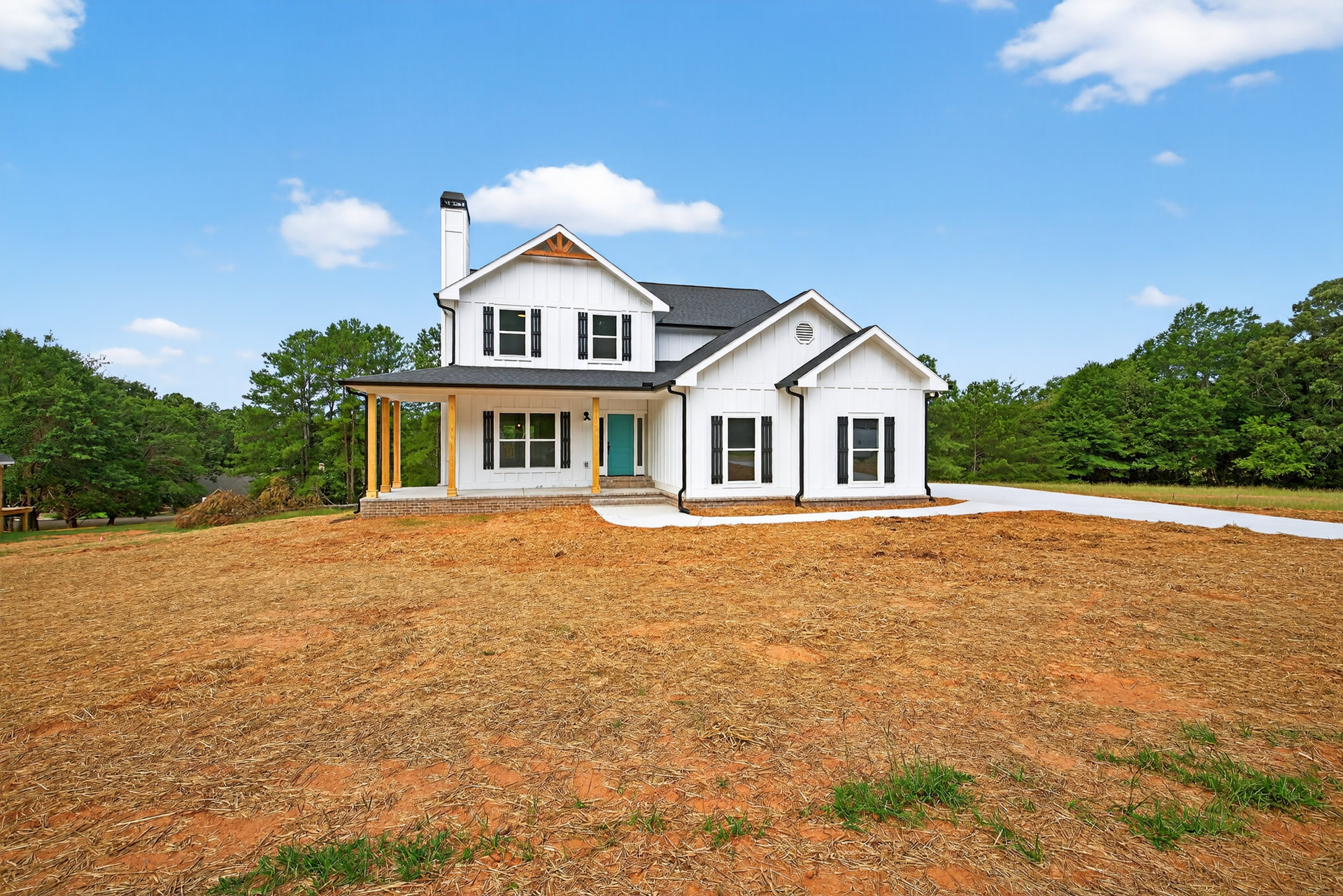 White two-story house with blue front door, large windows with white frames, expansive grassy yard, and mature trees under a clear blue sky