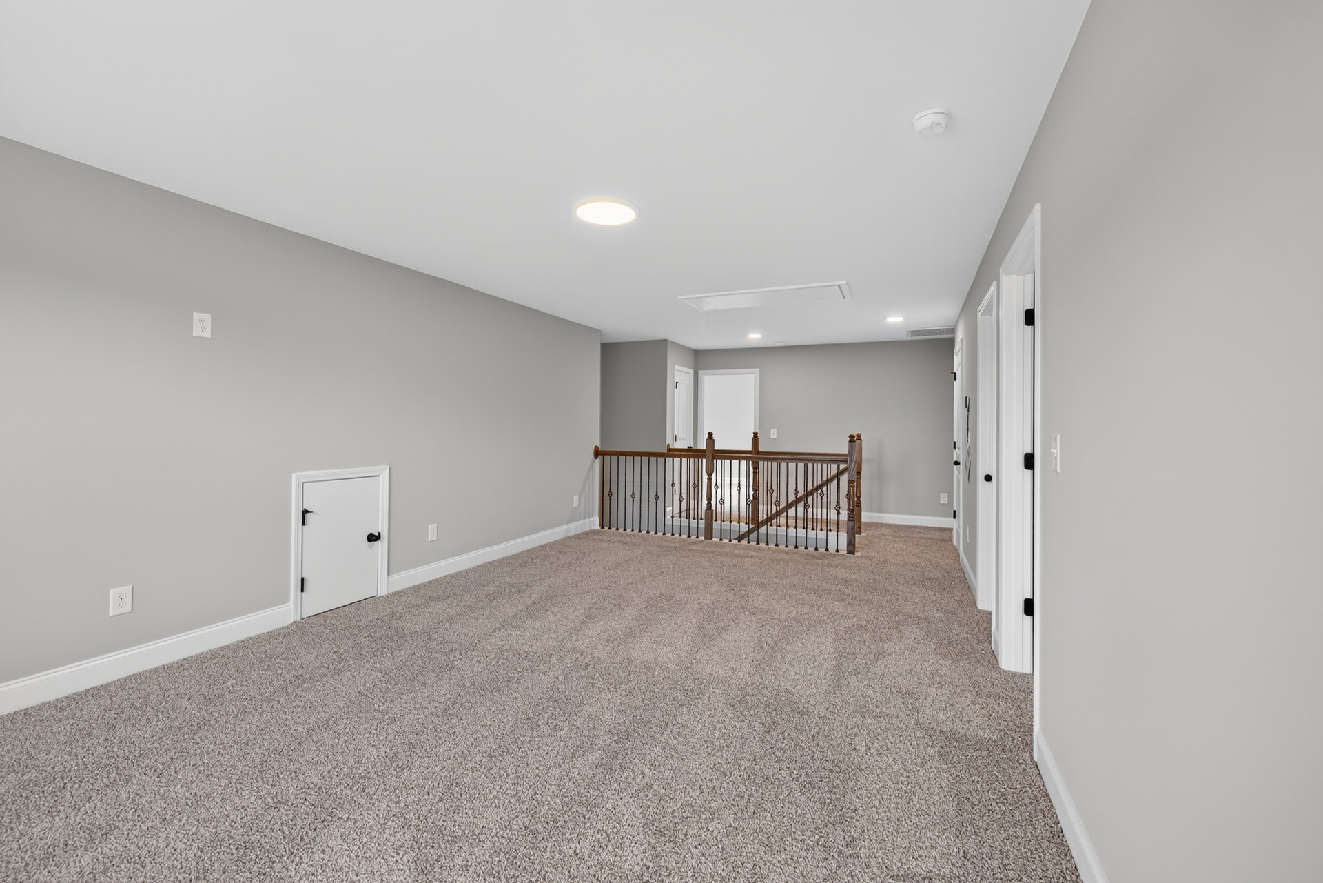 Carpeted floor with metal railing staircase, white door with black handles, ceiling light fixture, white walls, wood trim