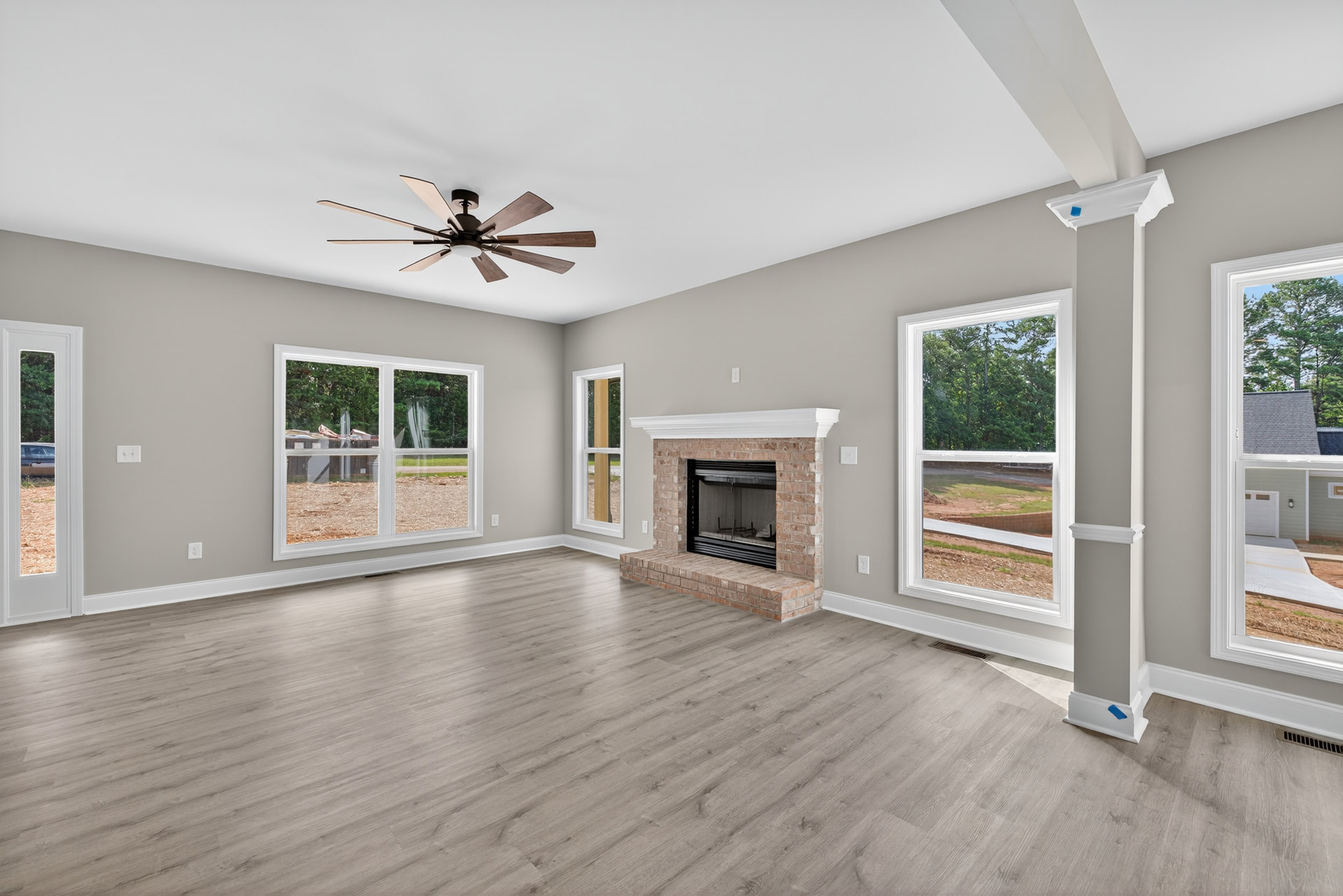 Living room with wood flooring, stone fireplace, ceiling fan with wood blades, large window, upholstered chair, neutral walls