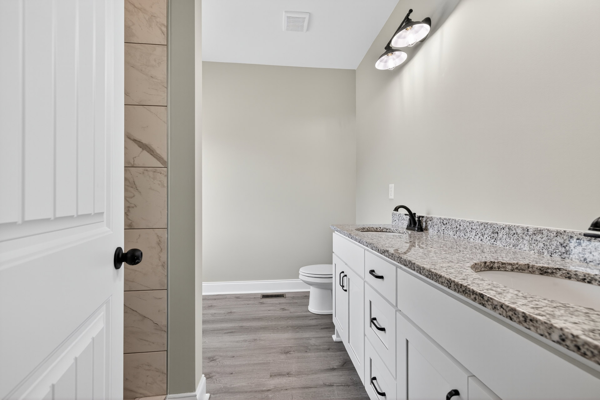 Bathroom with white cabinetry, marble countertop, undermount sink, chrome faucet, toilet, tile flooring, ceiling vent, and modern light fixture