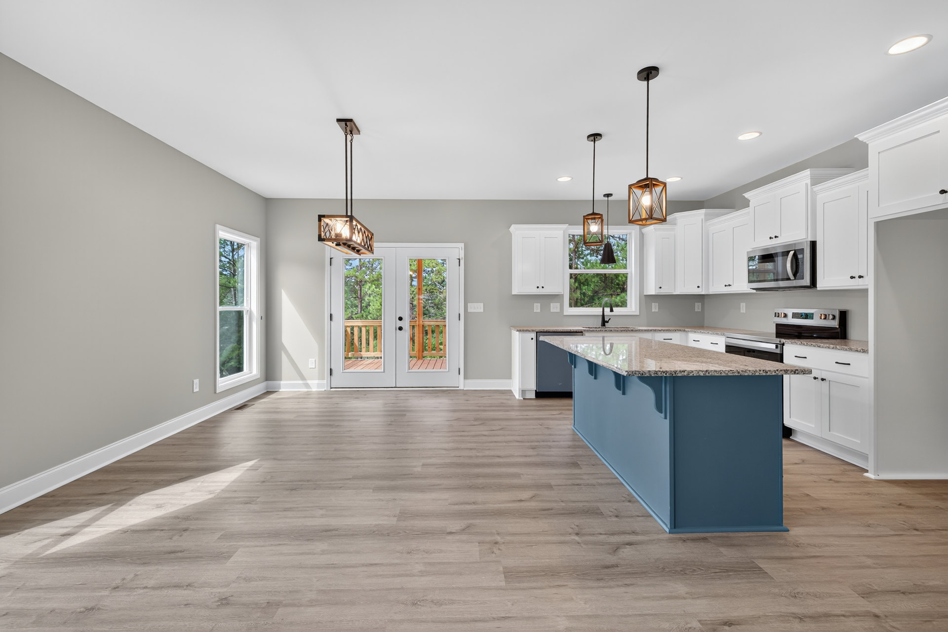 Kitchen with wood flooring, central island featuring granite countertops, white cabinetry, glass-paneled double doors, window with cracked glass, built-in white microwave, and a