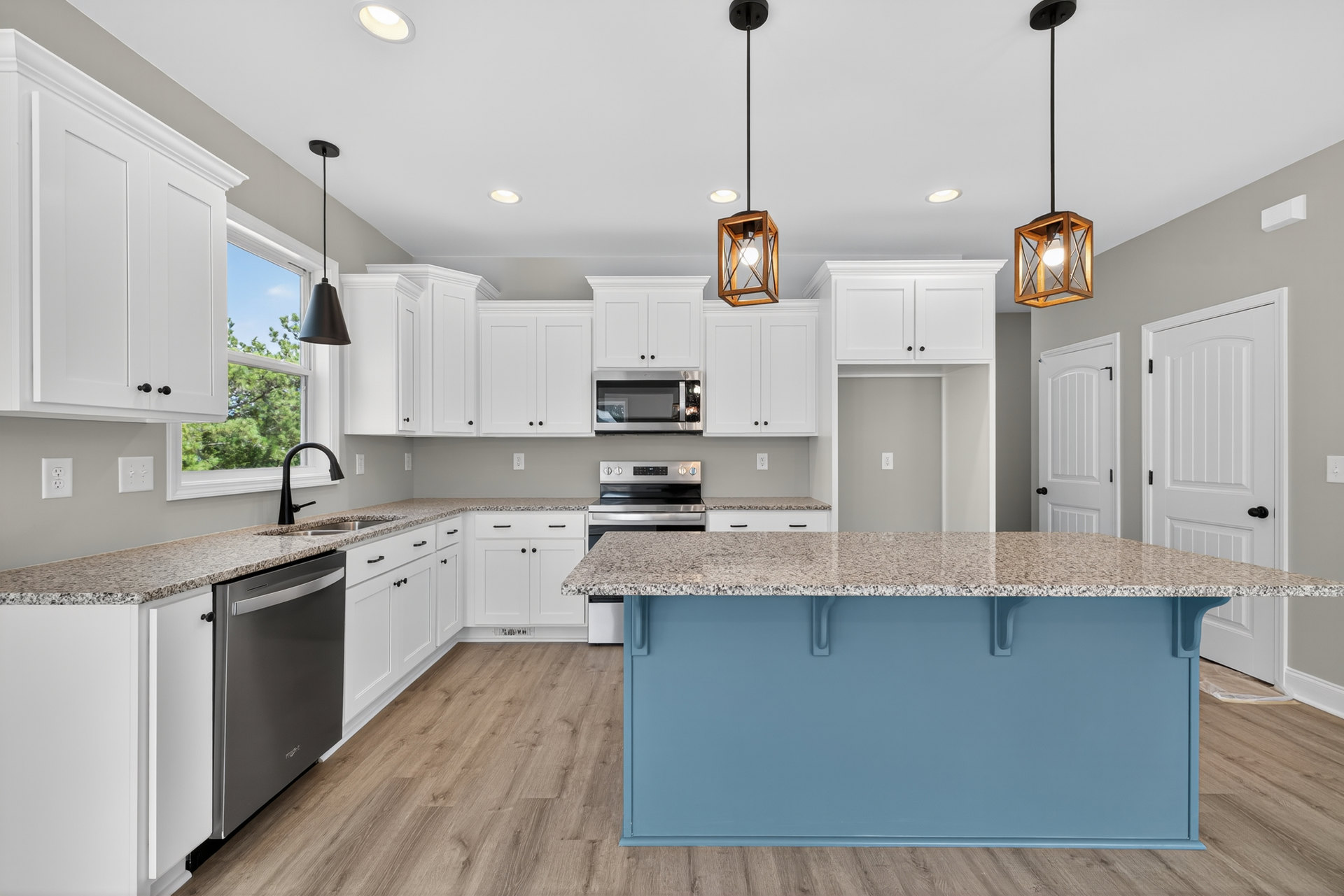 Blue kitchen island with white shaker cabinets, black refrigerator, quartz countertops, pendant light fixture, stainless steel sink, and built-in microwave.