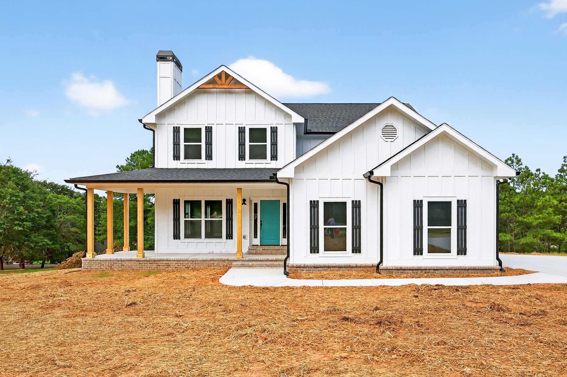 White siding house with blue front door, black railing along porch, windows with white trim, tree with green leaves in foreground, cloudy sky overhead.