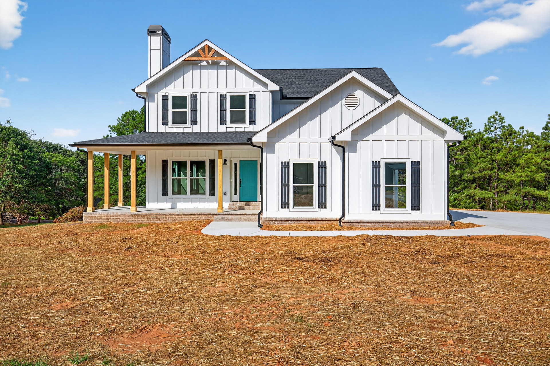 White siding home with blue front door, white-framed windows, covered porch, green lawn, and mature trees under partly cloudy sky