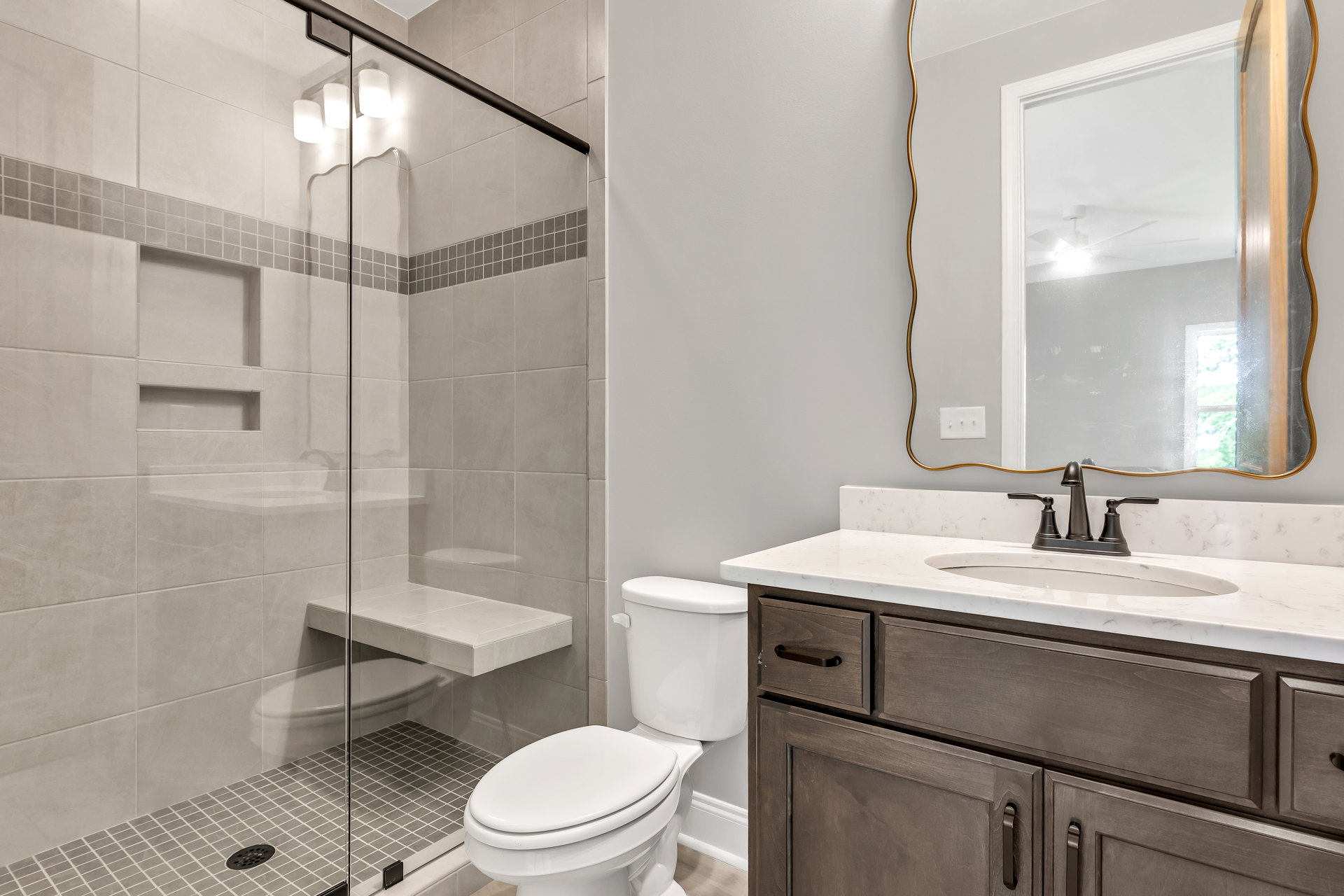 Bathroom with glass shower enclosure, white tile floor, modern sink with chrome faucet, curved-edge mirror above countertop, and closed white toilet.