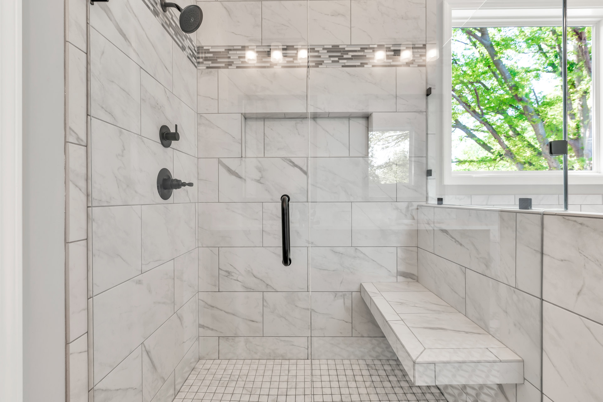 White tiled shower featuring a built-in bench, black metal shower fixtures, and a window letting in natural light.