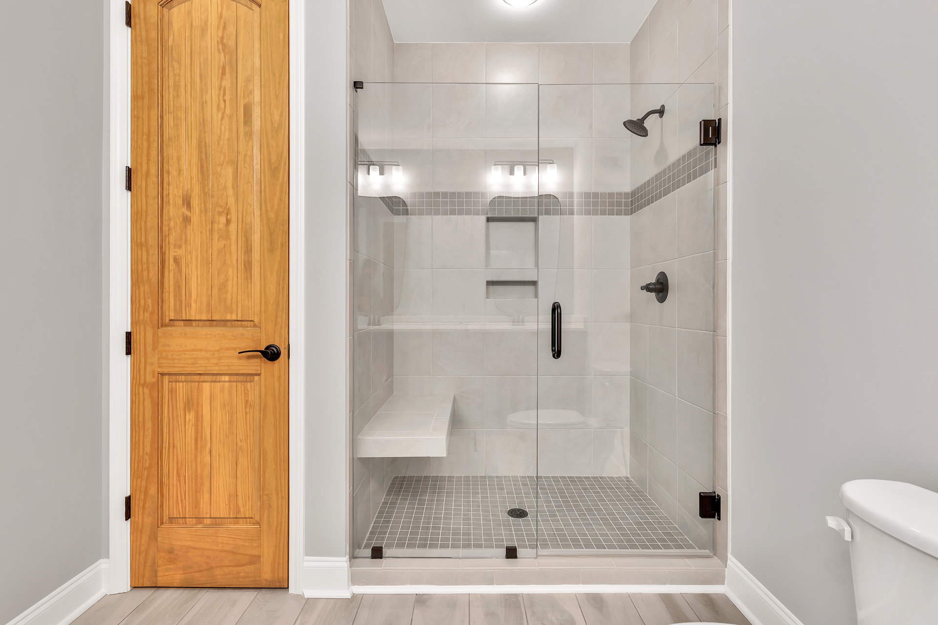 Glass shower enclosure with built-in bench, wood door, tile walls, and modern plumbing fixtures