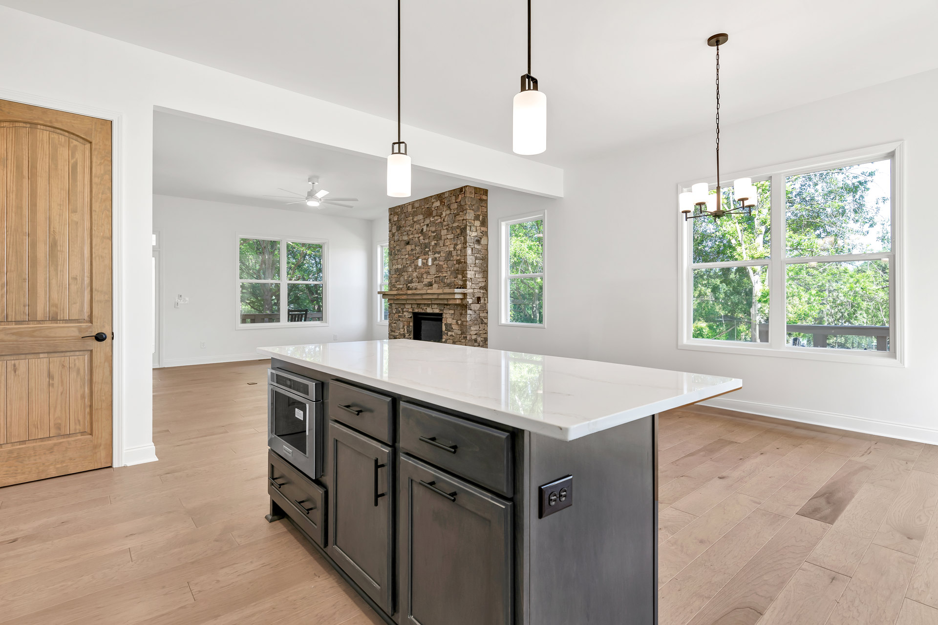 Quartz kitchen island with waterfall edge, built-in sink, matte gray cabinetry, stainless steel microwave, pendant light fixture, light wood flooring, and black hardware on doors