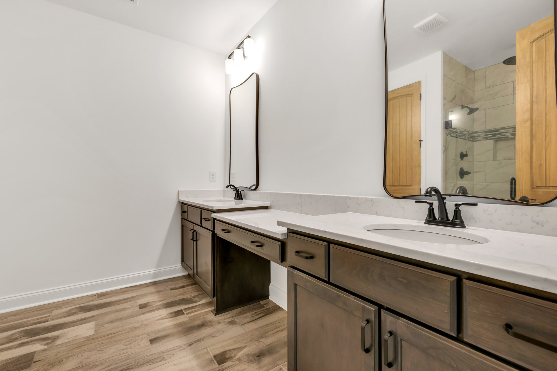 Bathroom with two undermount sinks set in a light stone countertop, wide black-framed mirror above, white walls, modern chrome faucets, and dark wood cabinetry below.
