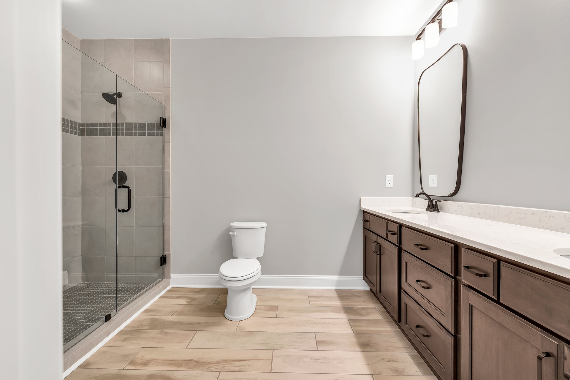 Modern bathroom with glass shower enclosure, chrome door handle, white toilet, light-colored walls, and tiled flooring