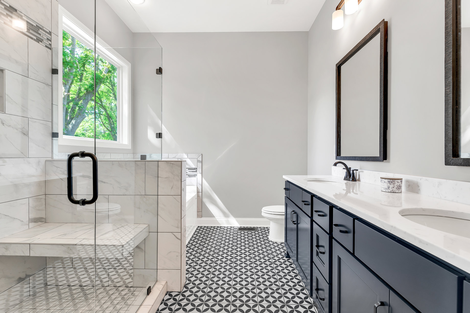 Bathroom with black and white tile floor, glass shower enclosure, white sink vanity, window overlooking trees, chrome fixtures, and close-up views of railing and toilet.
